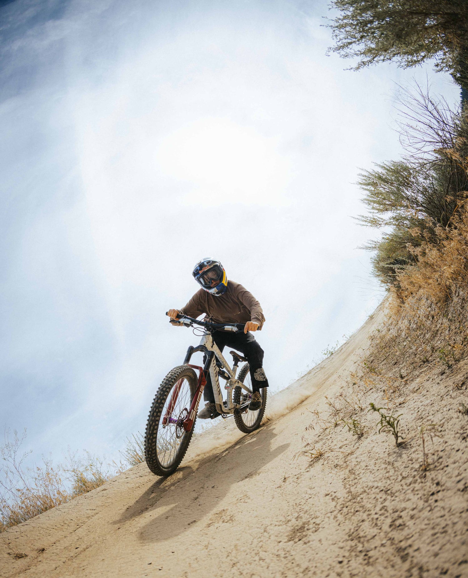 Person riding a mountain bike on a dirt trail with a clear sky and trees in the background
