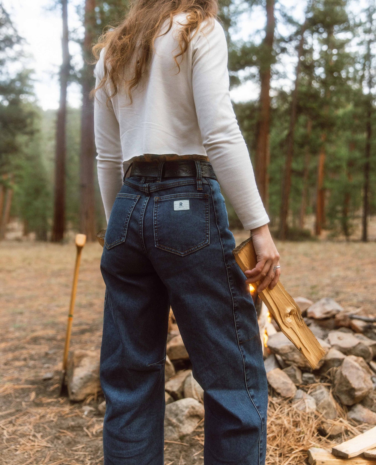 Person wearing blue jeans and a white long-sleeve shirt in a forest setting.