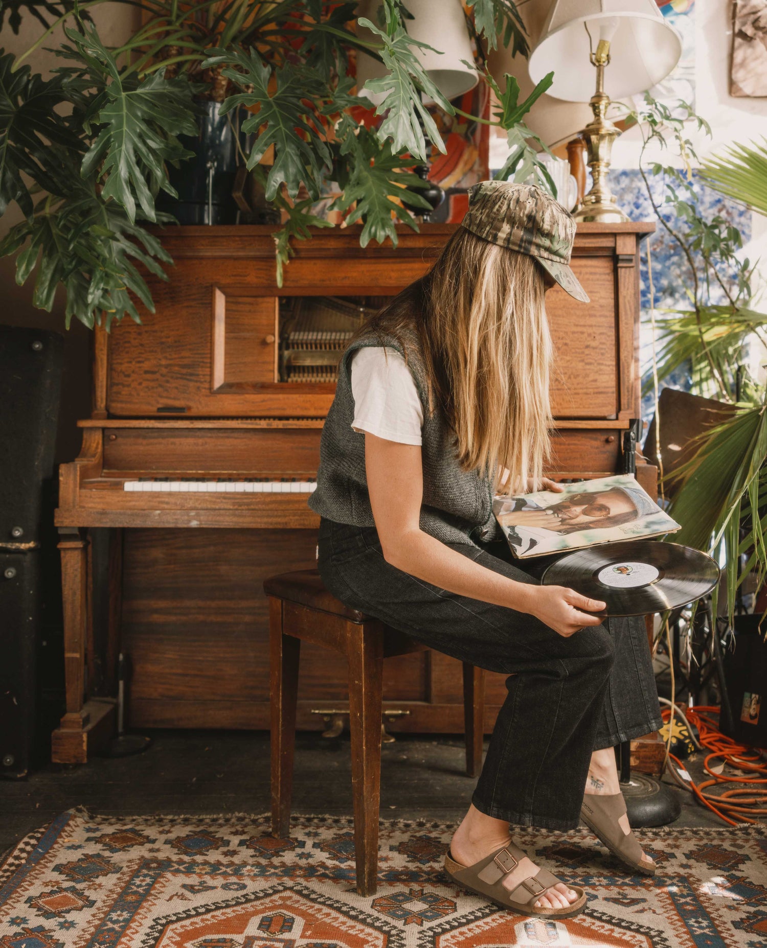 Person sitting at a piano surrounded by plants in a cozy room.