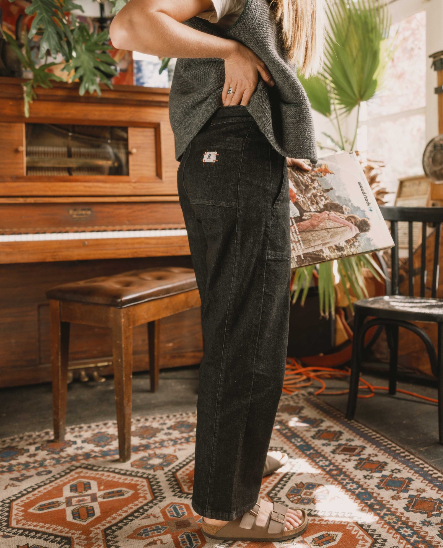 Person wearing dark pants and a gray sweater standing in a room with a piano and patterned rug.