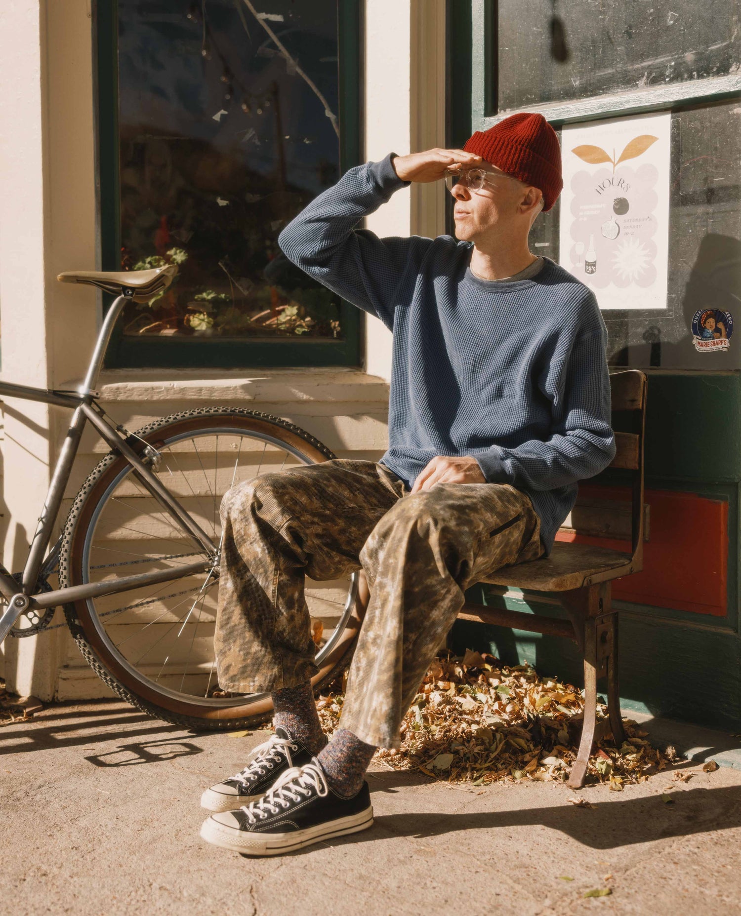 Person sitting on a chair next to a bicycle, wearing a blue sweater and red beanie.