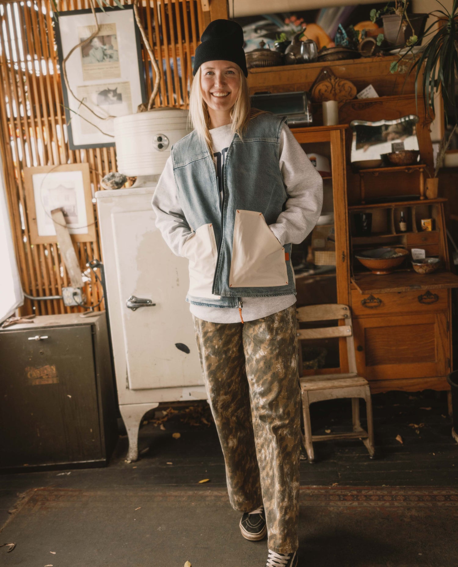 Person wearing a denim vest and camouflage pants in a rustic indoor setting