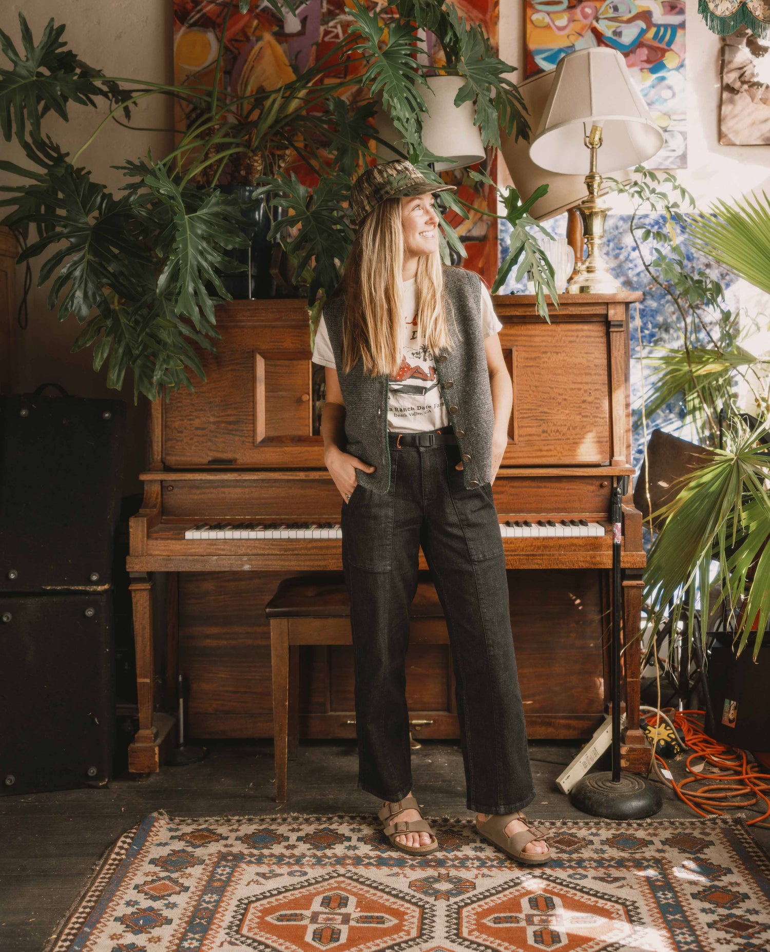 Person standing in a room with a piano, plants, and colorful wall art.