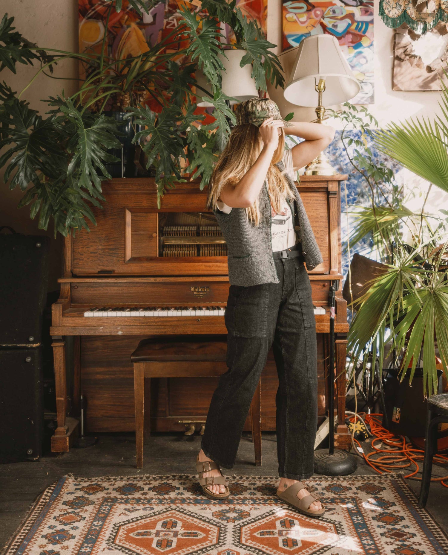 Woman standing in a room with a piano, plants, and colorful wall art.