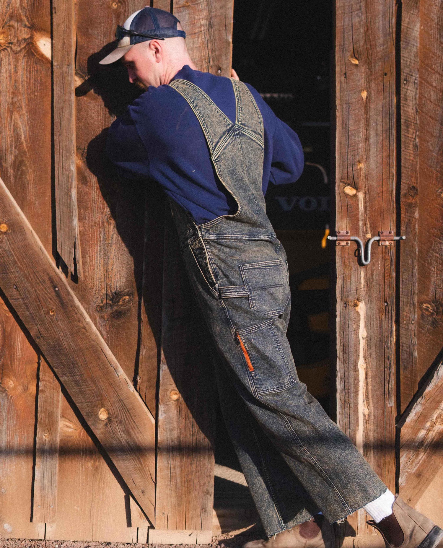 Man pushing open barn door in Starving Jartist Overalls.