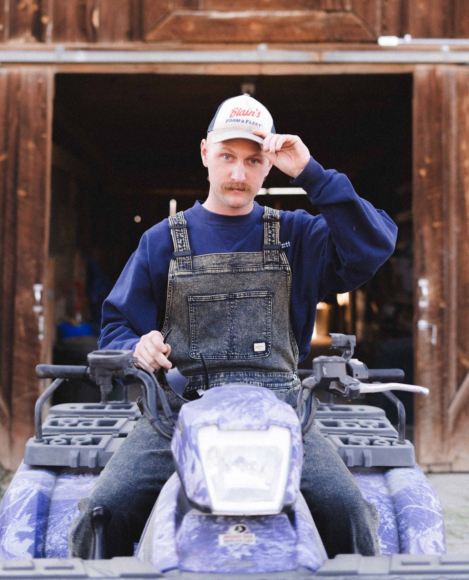 Man sitting on an ATV in Ripton Dirty Dave Starving Jartist Overalls.