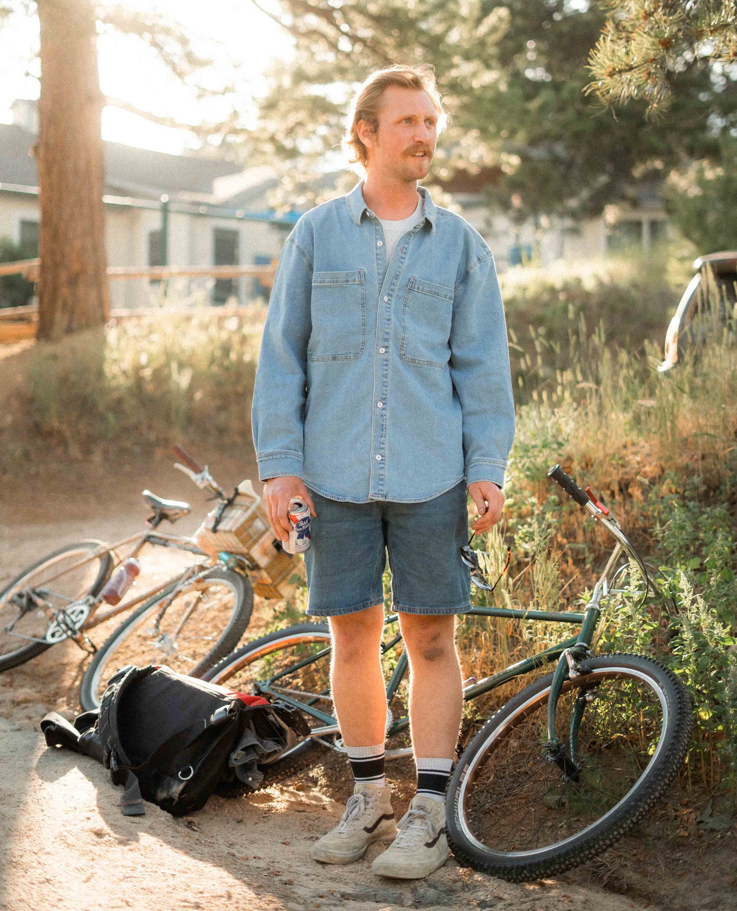 Man standing outdoors with bicycles, wearing a light blue shirt and shorts.
