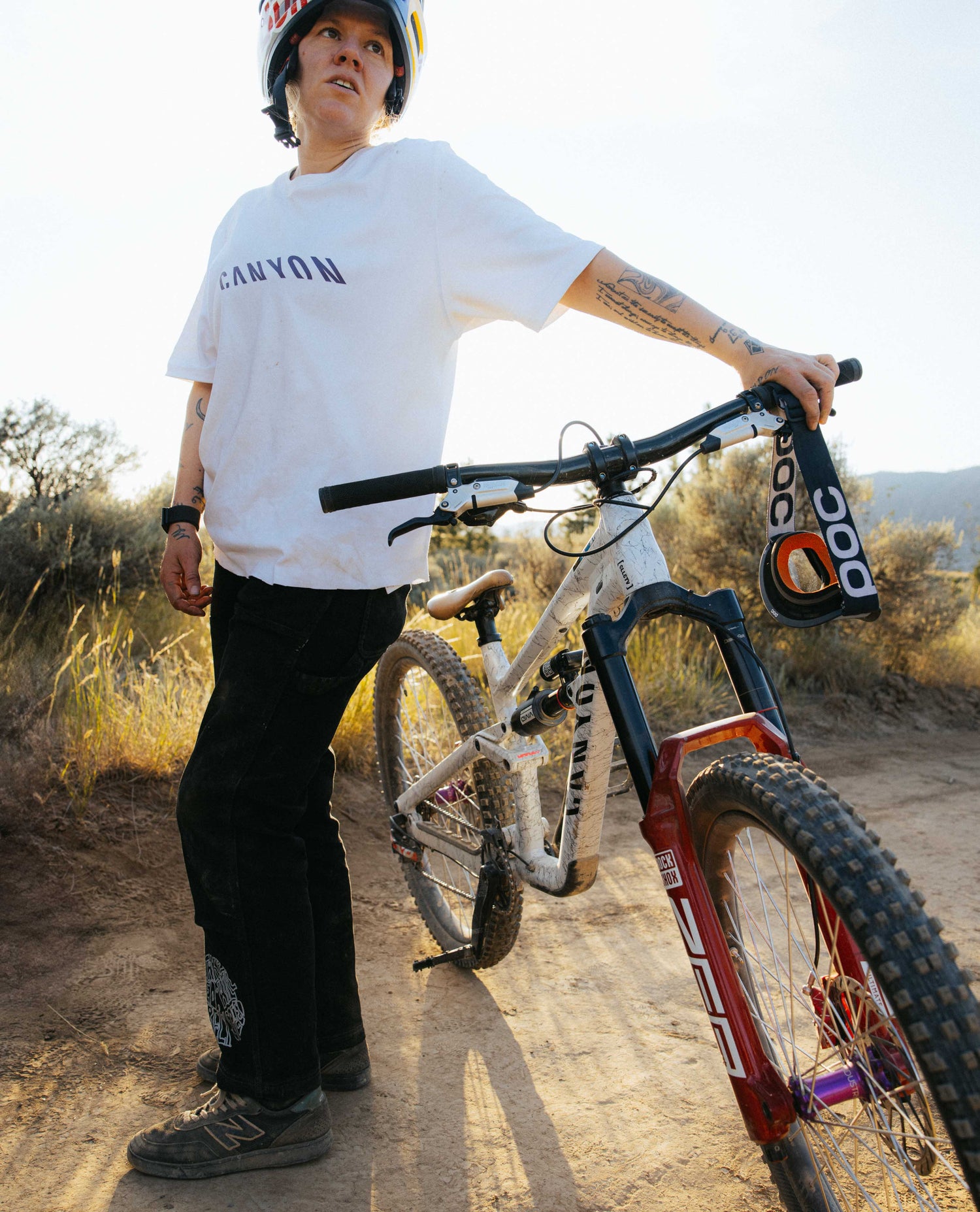 Person standing next to a mountain bike on a dirt trail with a scenic background