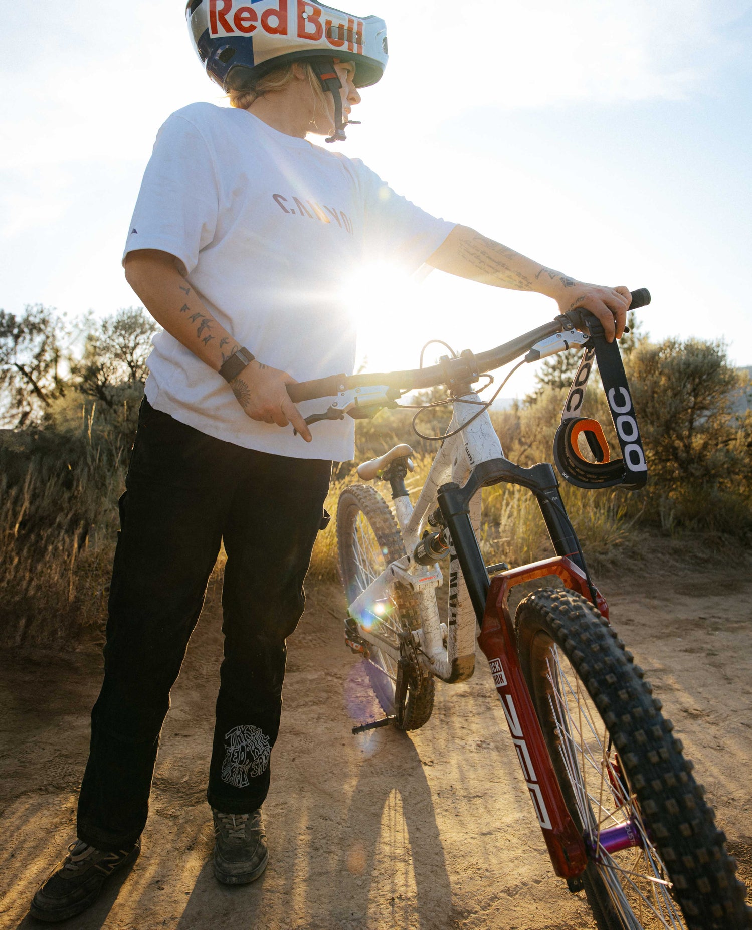 Person with a mountain bike on a dirt path, wearing a helmet with 'Red Bull' branding.