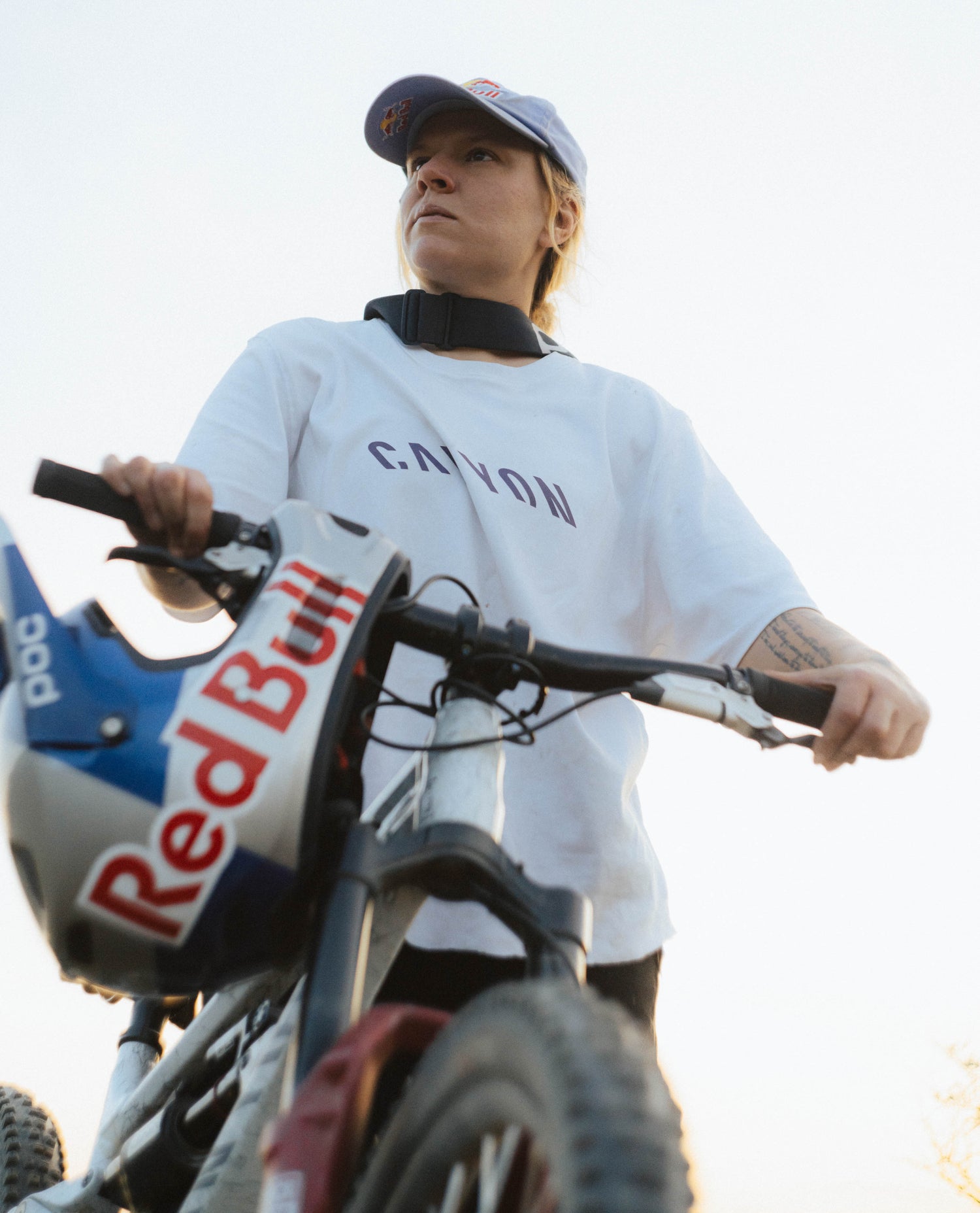 Person on a bike with a helmet and 'Red Bull' branding, wearing a white shirt with 'Caveman' text.