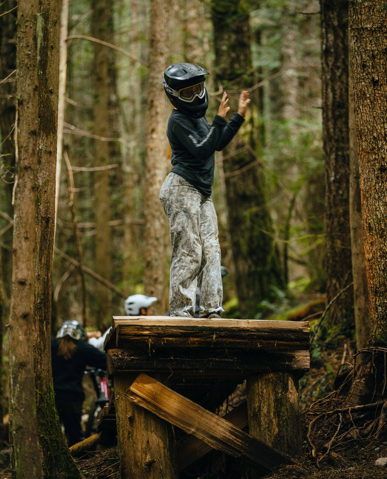Person on a wooden platform in a forest wearing protective gear