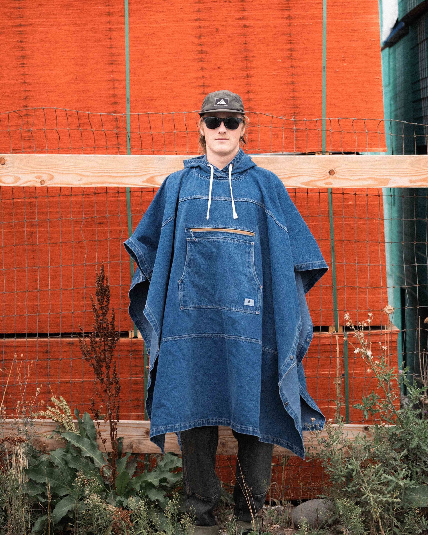 Person wearing a blue denim poncho in an outdoor setting with orange walls.