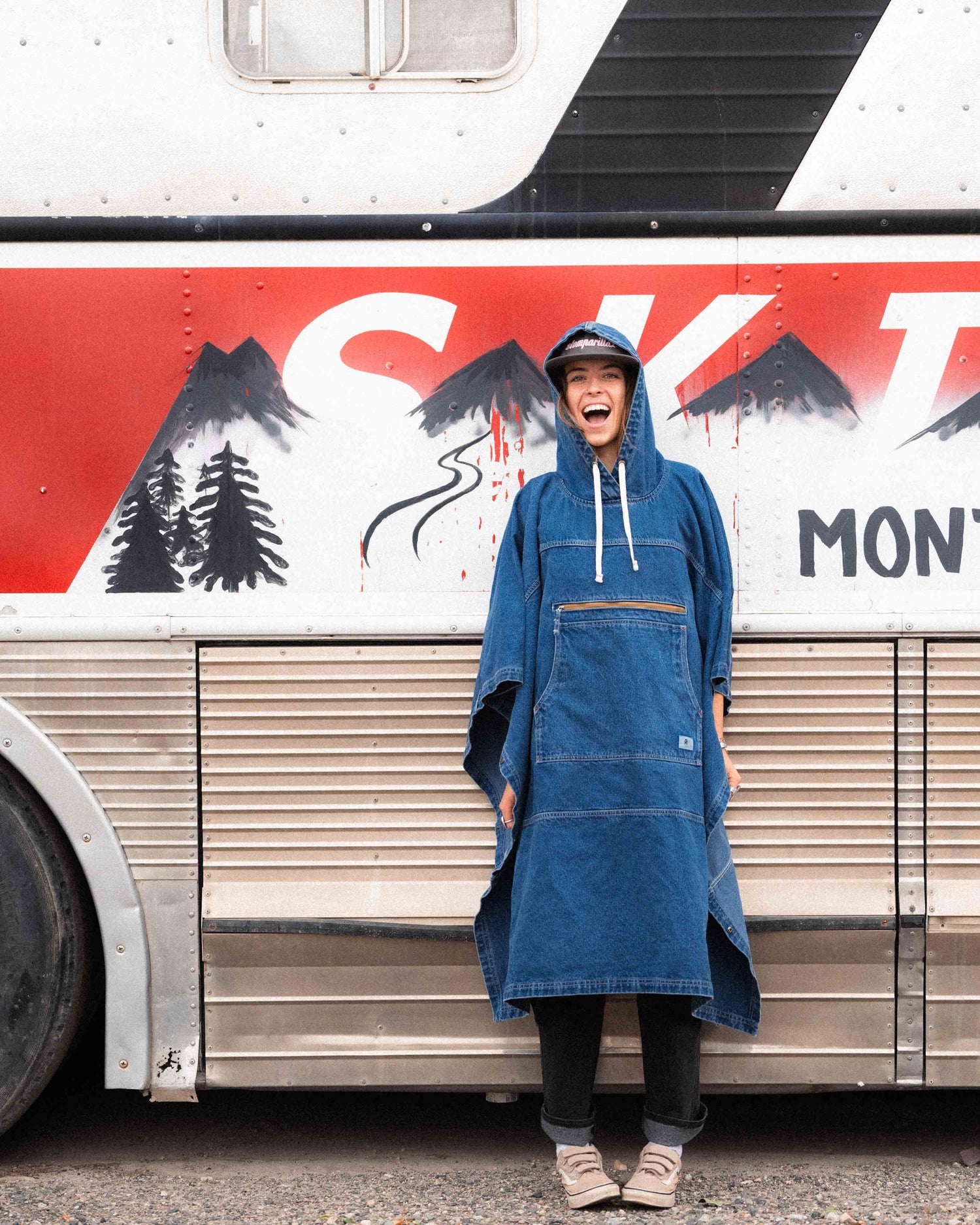 Person wearing a blue denim poncho in front of a trailer with mountain and tree design.