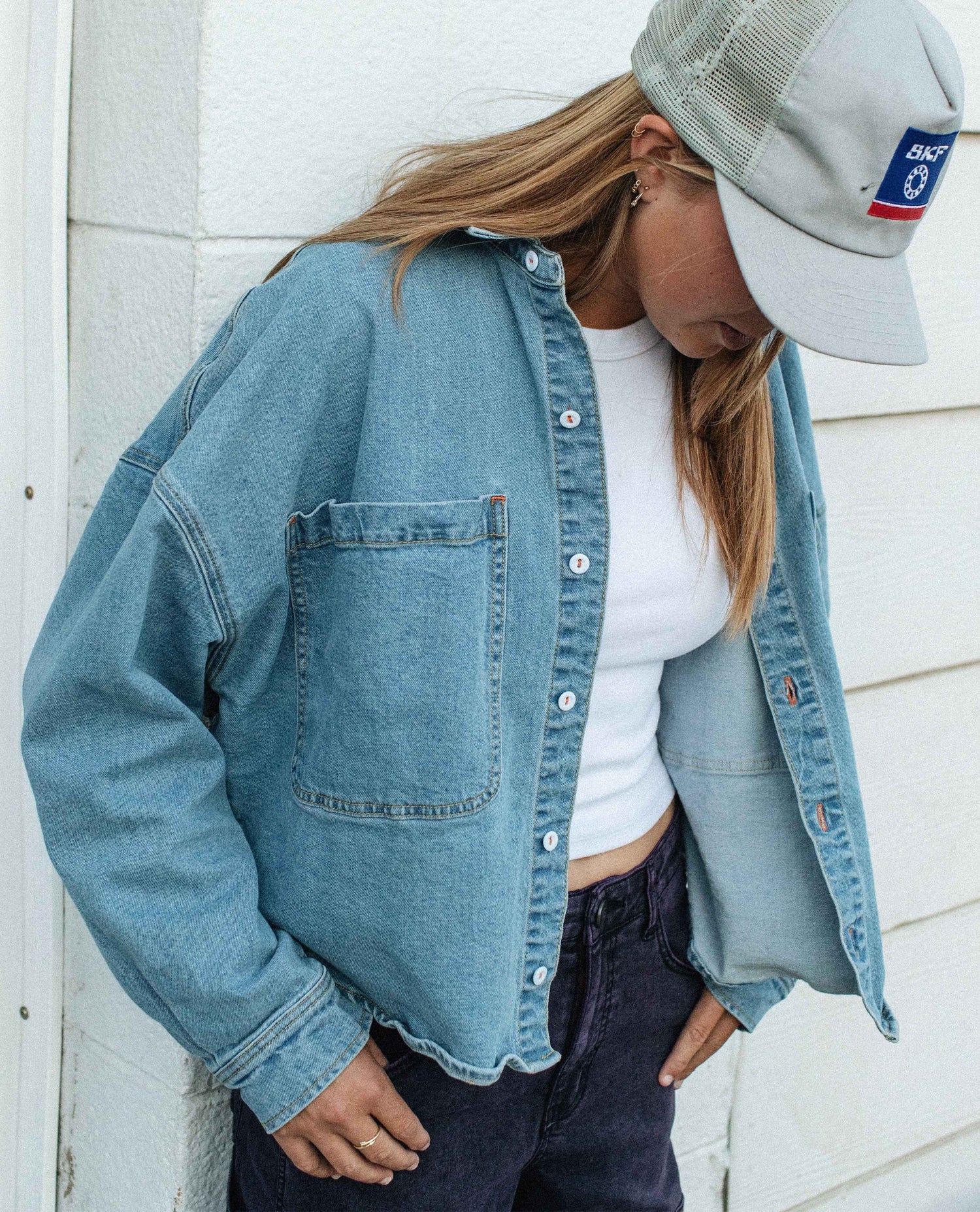 Person wearing a denim jacket, white shirt, and gray cap against a light-colored wall.