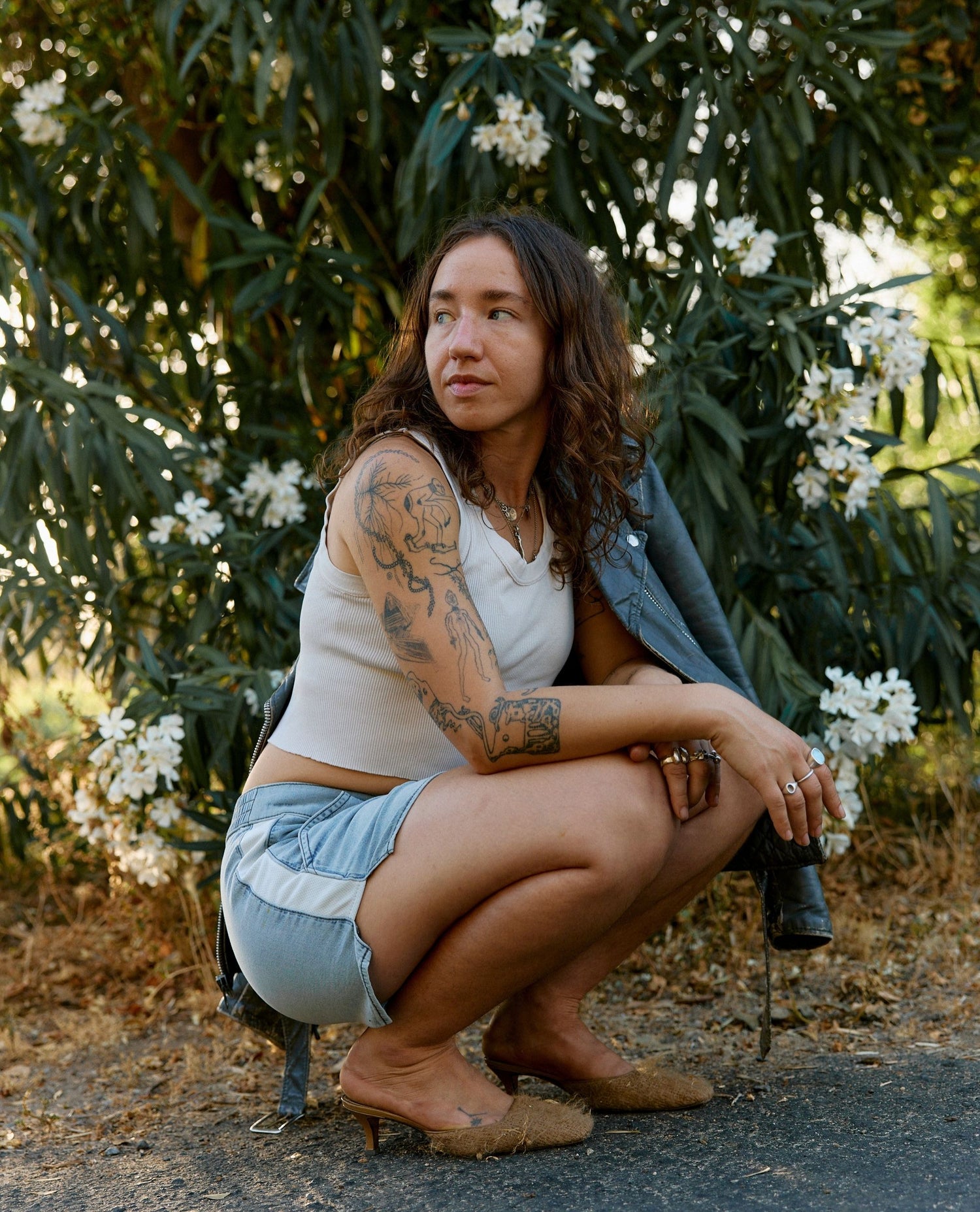 Woman squatting outdoors with greenery and white flowers in the background