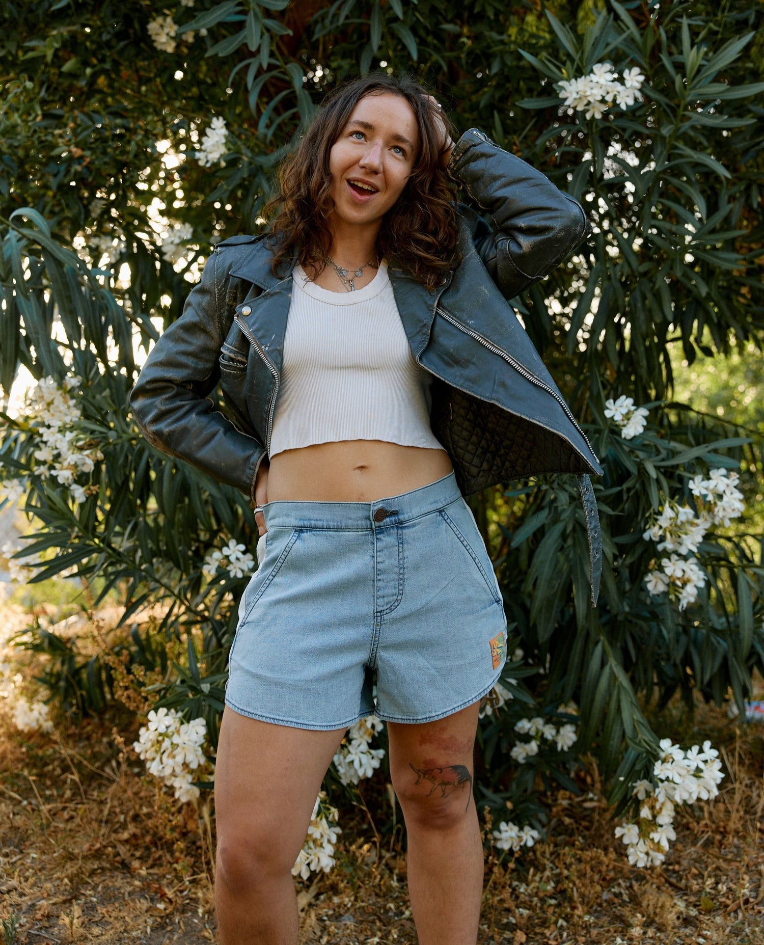 Woman standing outdoors with greenery and white flowers in the background