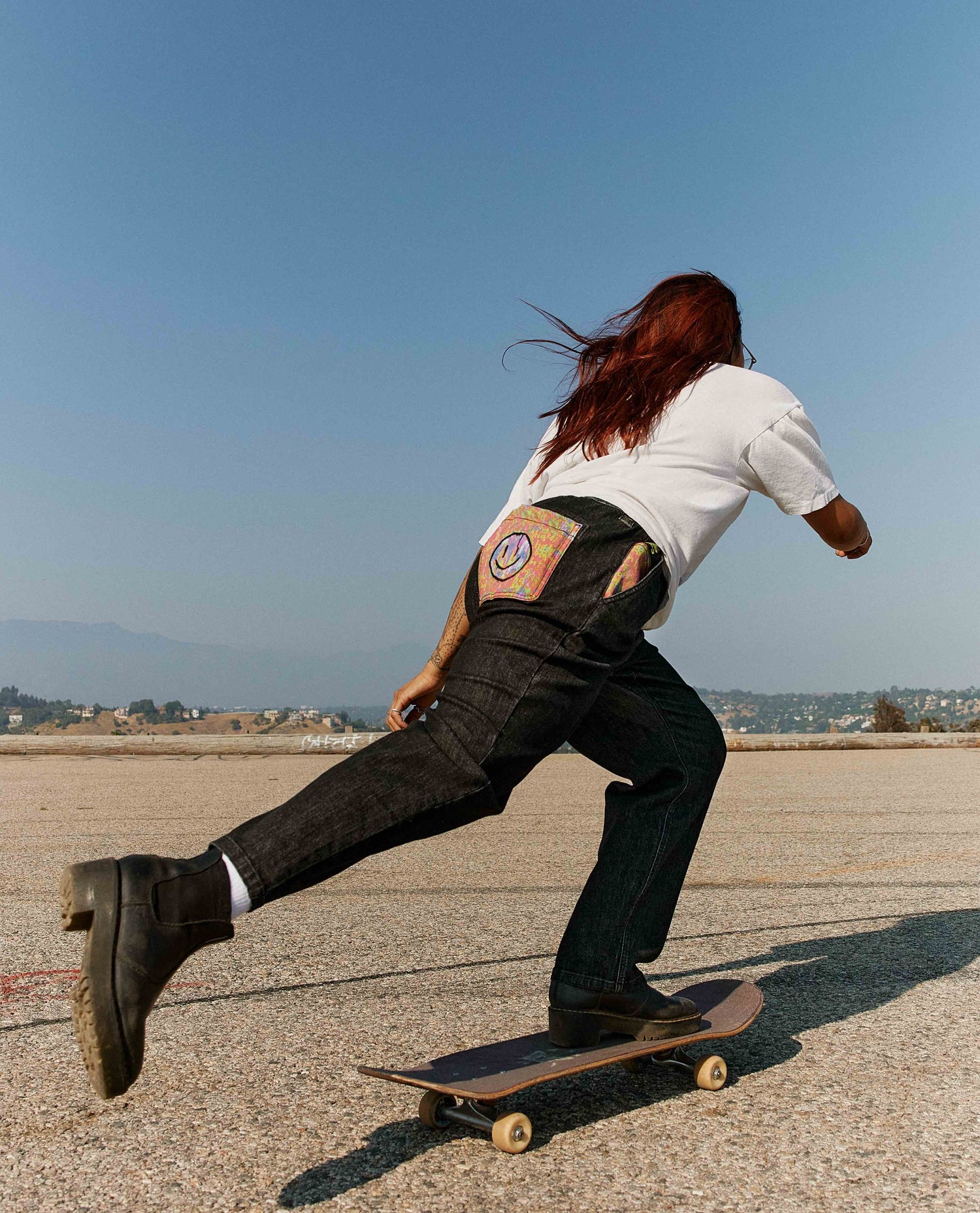 Woman pushing a skateboard in Ripton x 3dumb pants. 