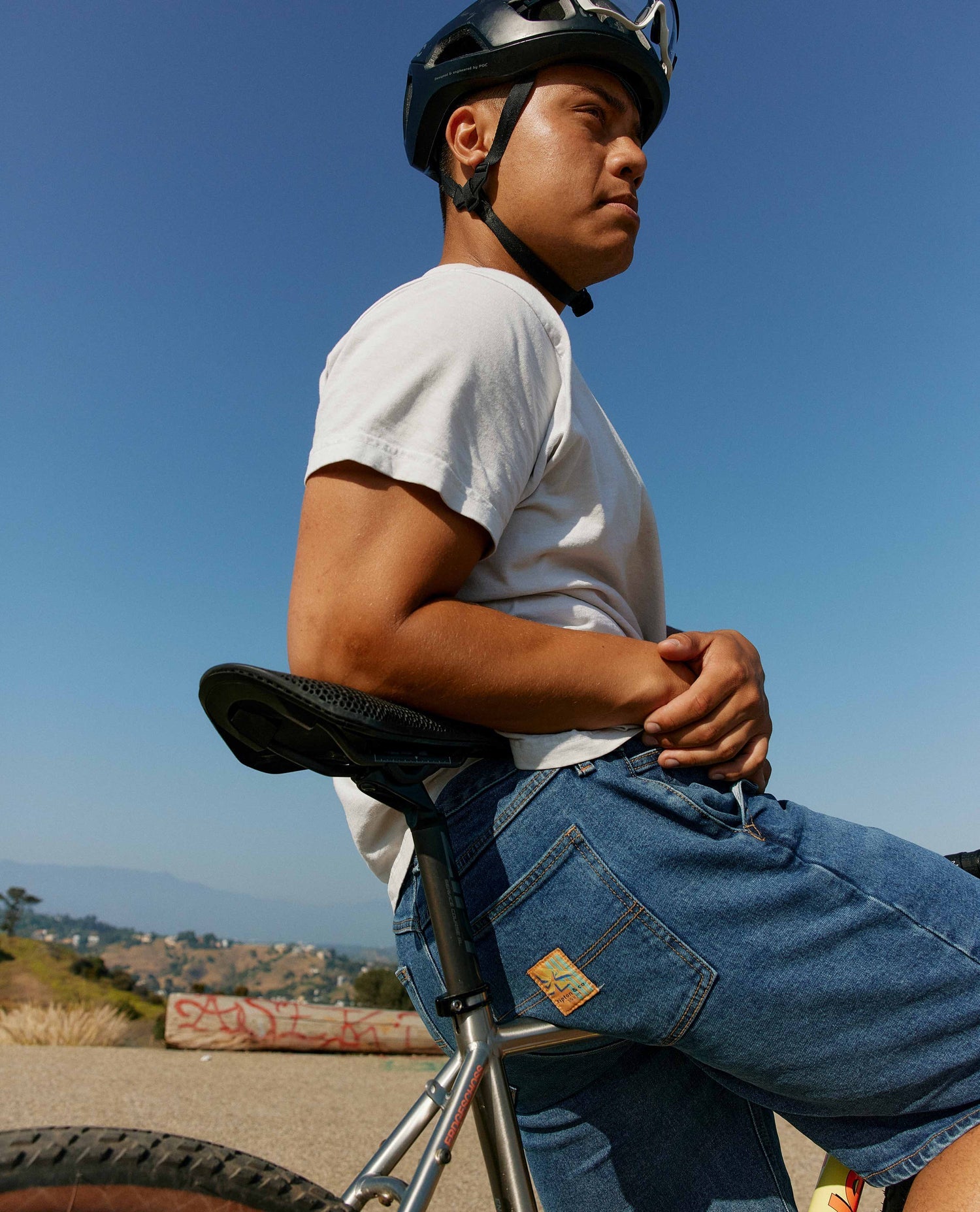 Mean wearing a white t shirt and jean shorts sitting on a bike.