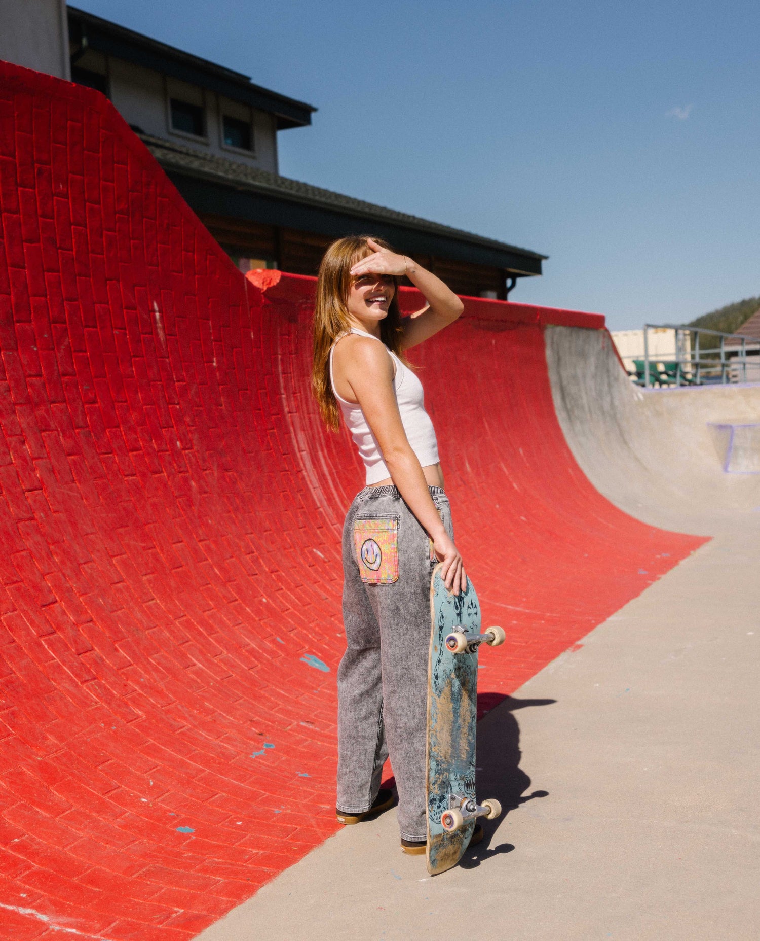 Woman standing in front of a red brick quarter pipe in Ripton 3dumb pants. 