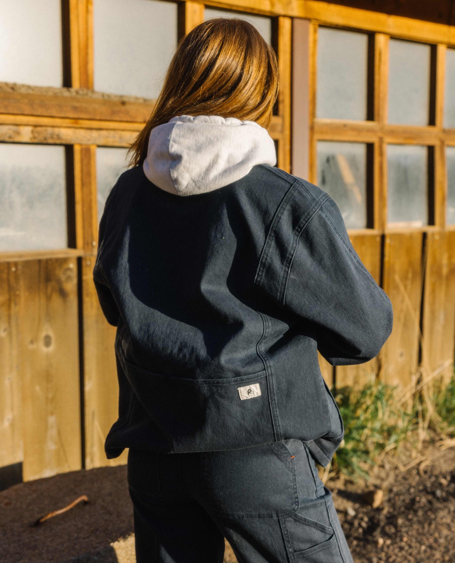 A woman facing away from the camera in front of an old building. She is wearing a blue cargo style jacket and pants as well as a light grey hoodie. 