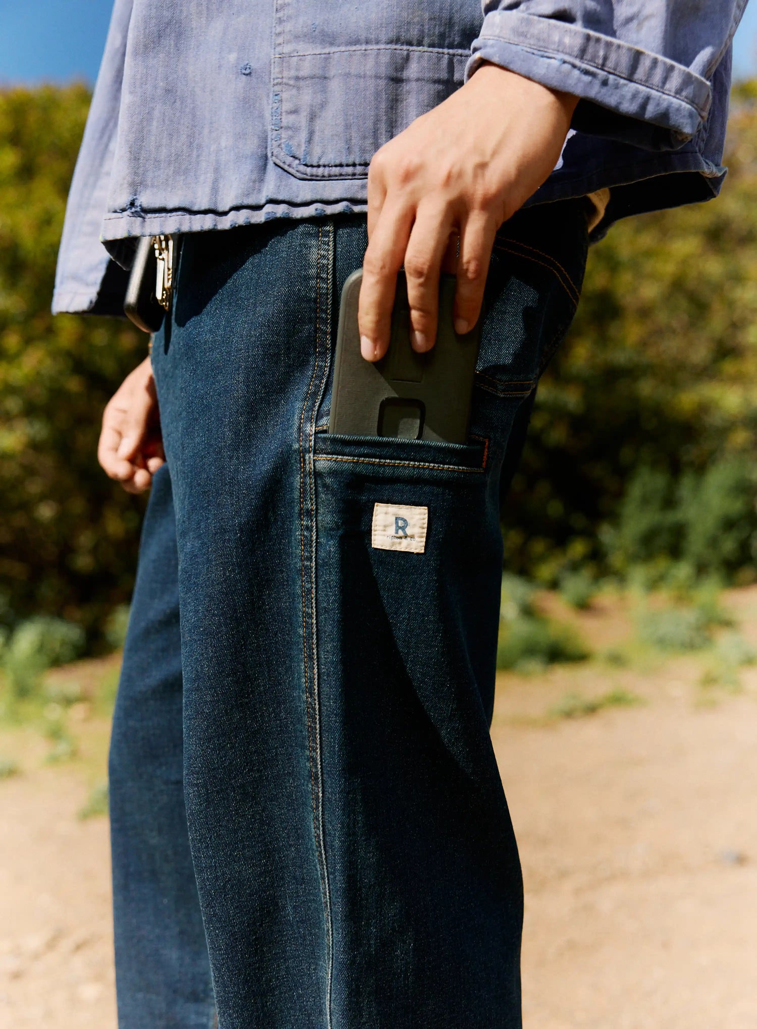 Person wearing blue jeans with a visible brand logo, holding a phone in a pocket.