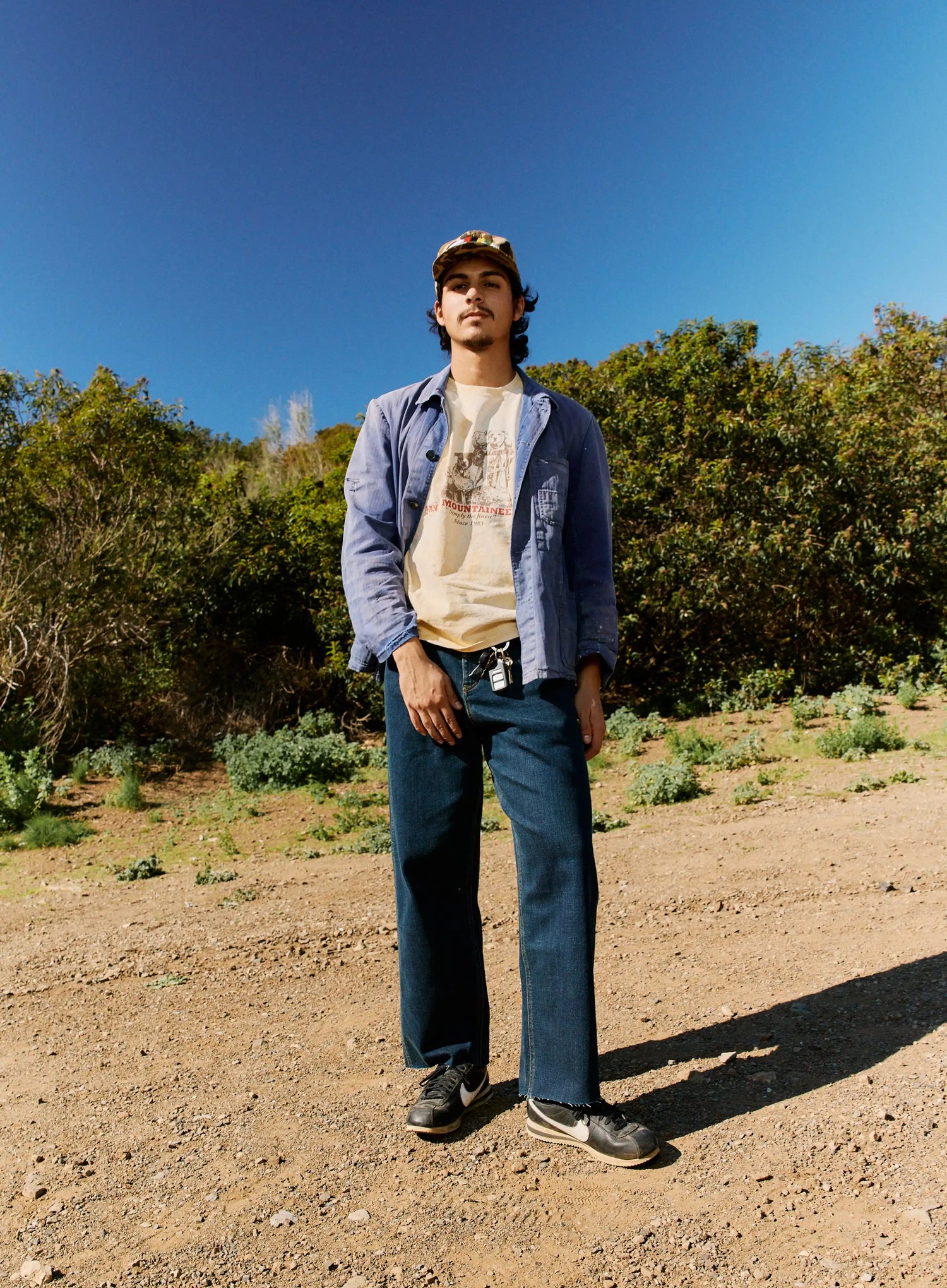 Person standing in a natural setting with trees and clear sky