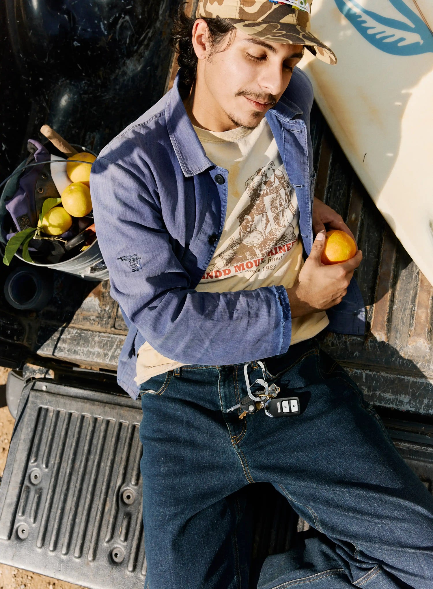Person holding an orange next to a truck with fruit in the background