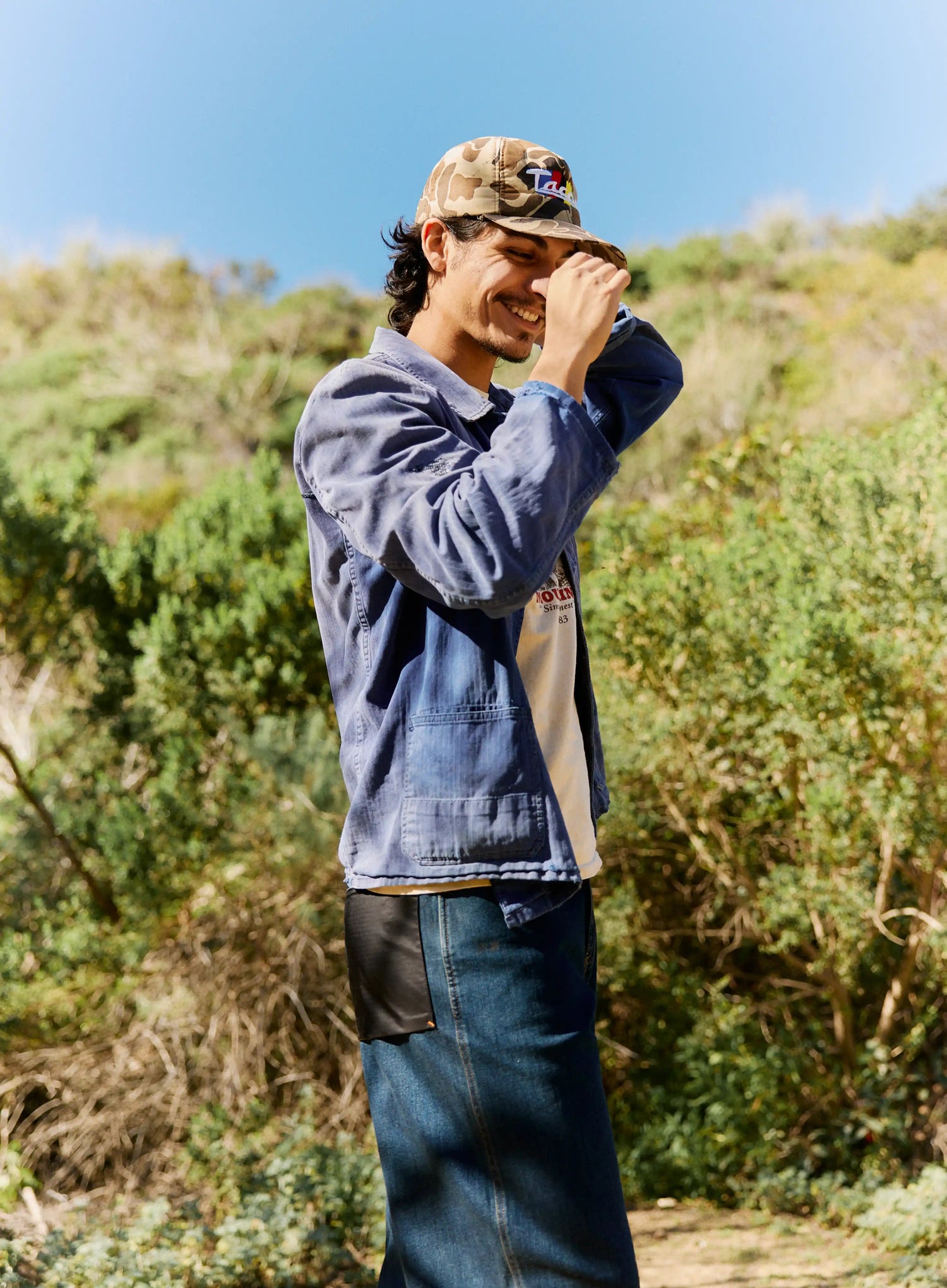 Person wearing a cap and denim jacket outdoors with greenery in the background