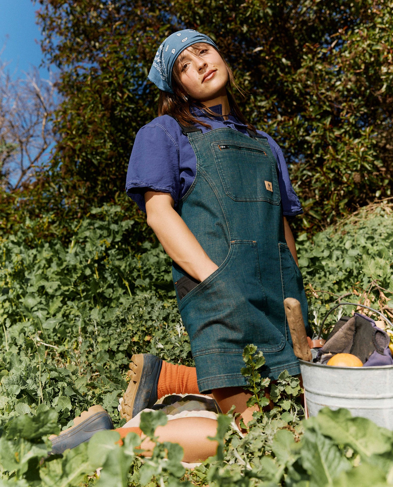Person wearing a blue apron and hat in an outdoor garden setting