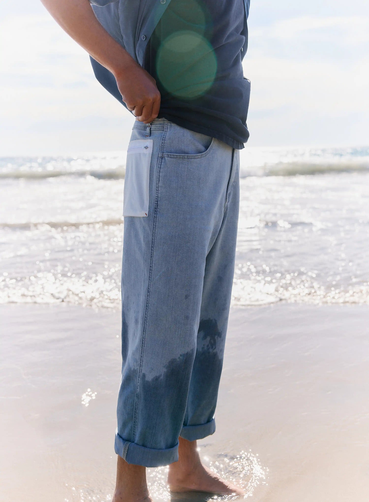 Person wearing a blue shirt and light blue jeans standing on a beach.