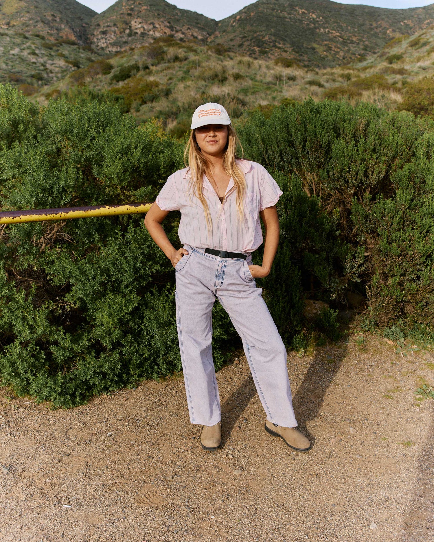 Person standing outdoors in a natural setting with mountains in the background