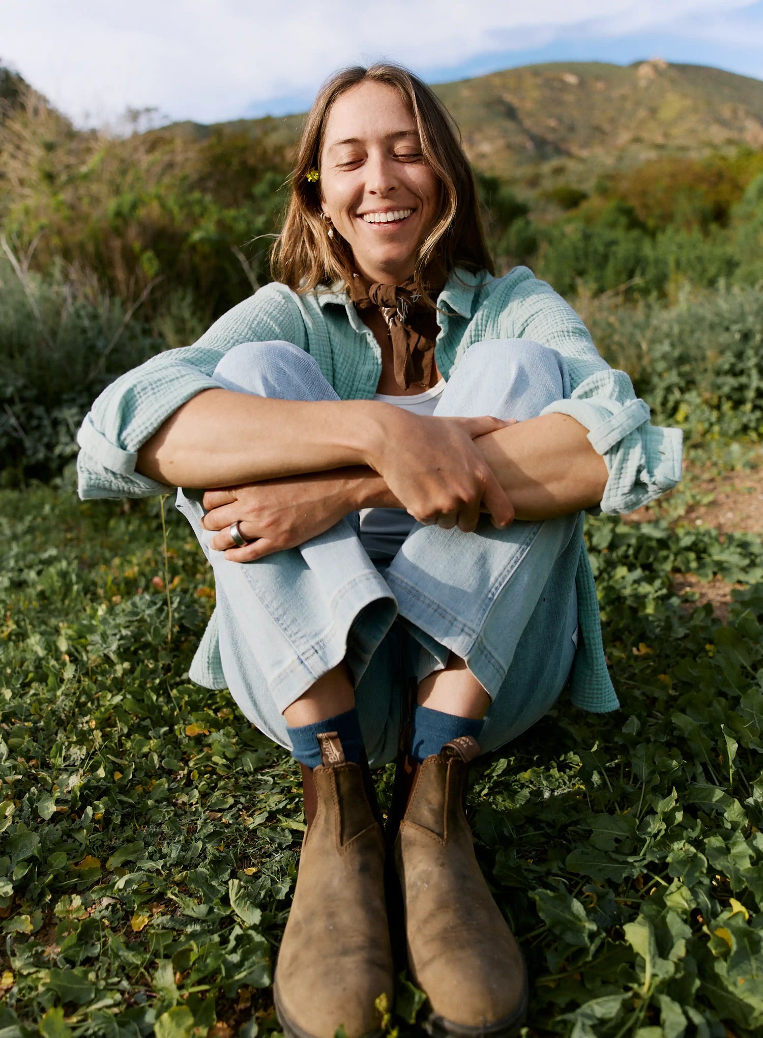 Woman sitting outdoors in a natural setting with mountains in the background