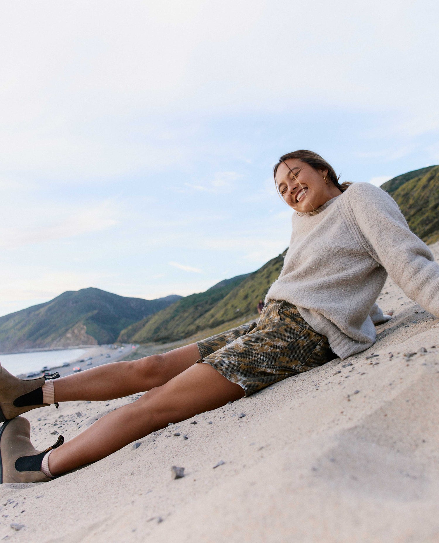 Person sitting on a sandy beach with mountains in the background