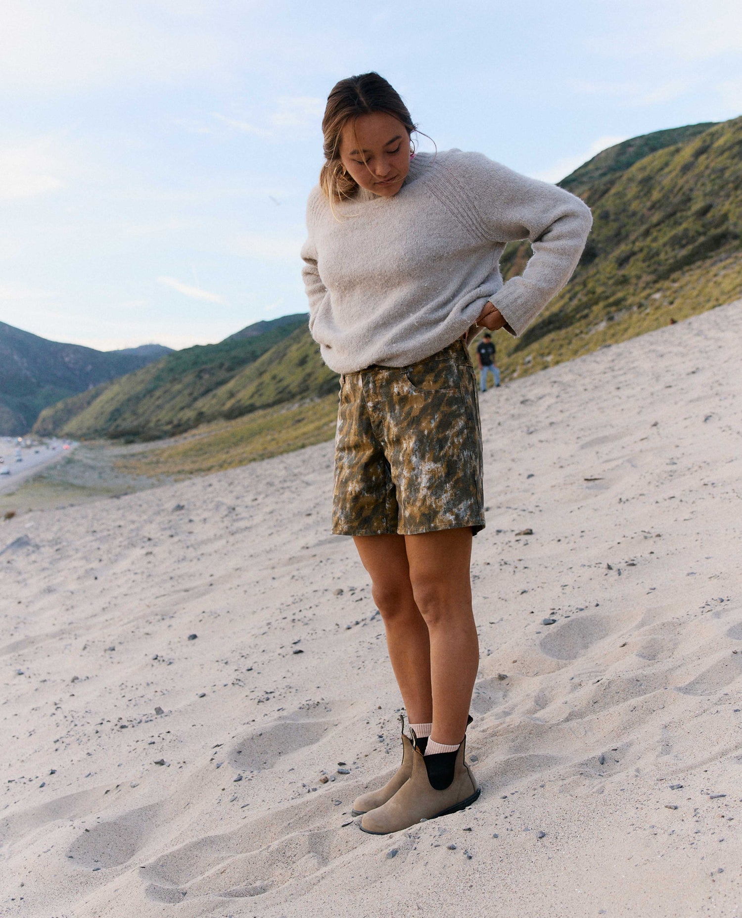 Person standing on a sandy beach with mountains in the background