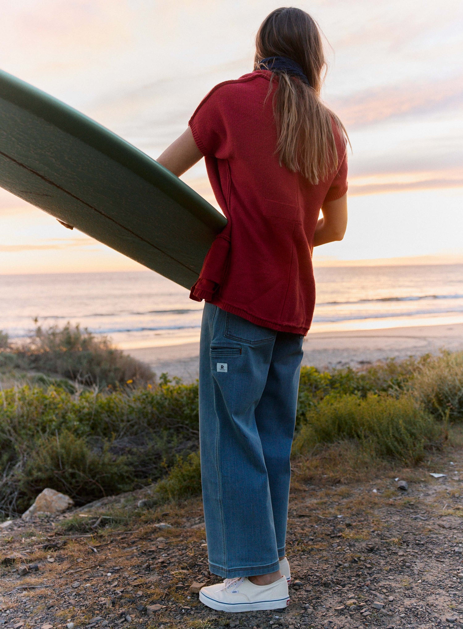 Person holding a surfboard, standing on a beach at sunset