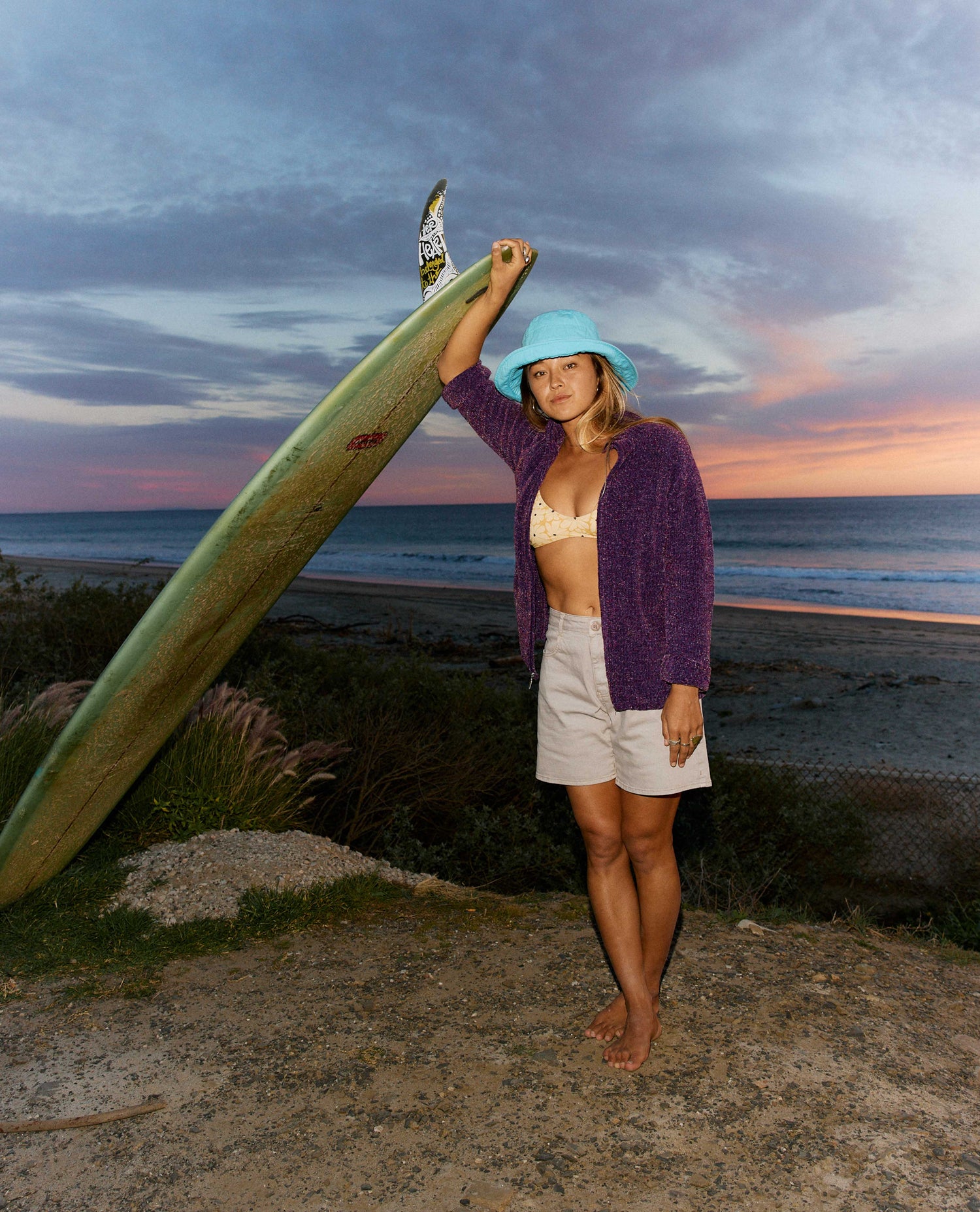 Woman holding a surfboard on a beach at sunset