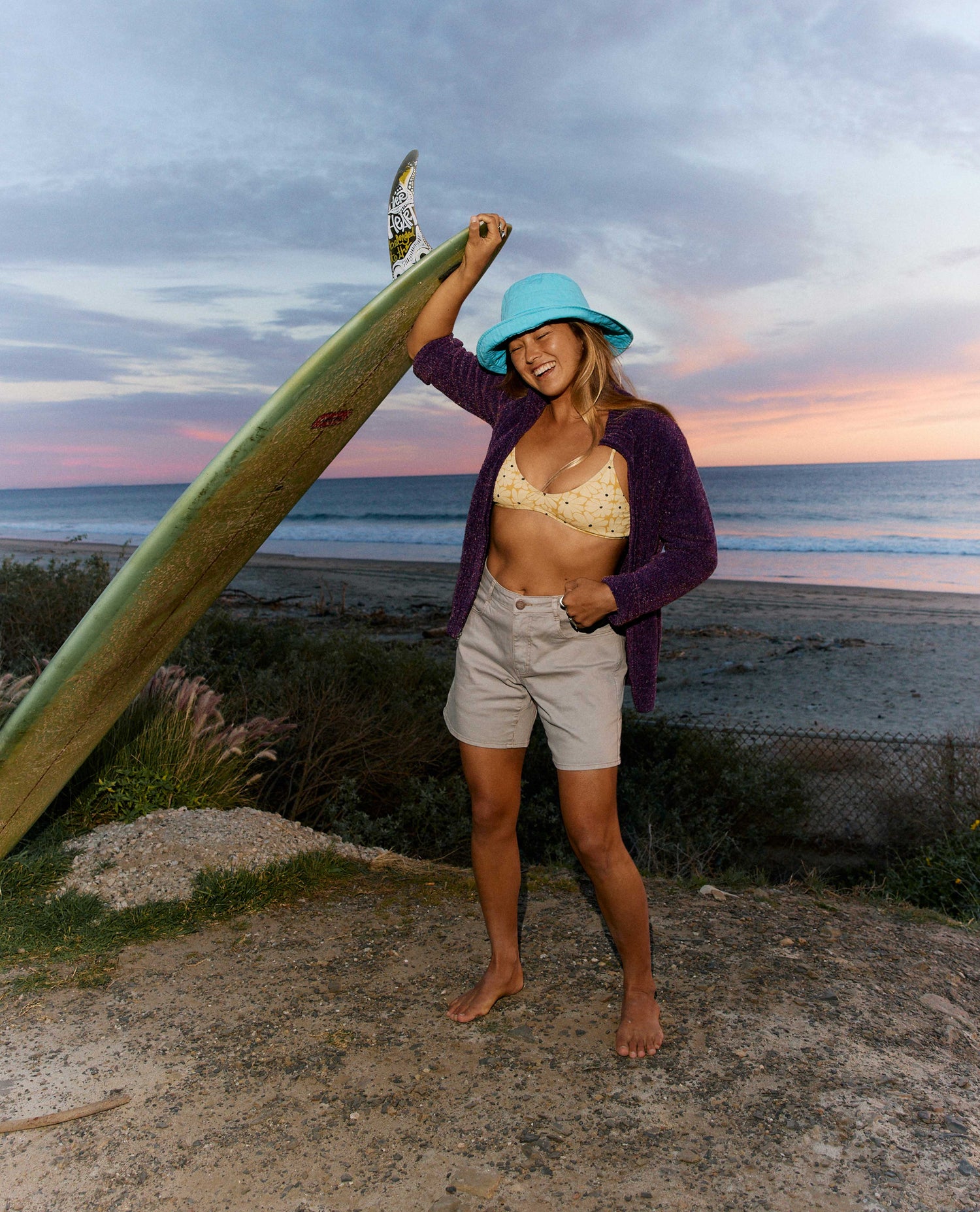 Woman holding a surfboard on a beach at sunset