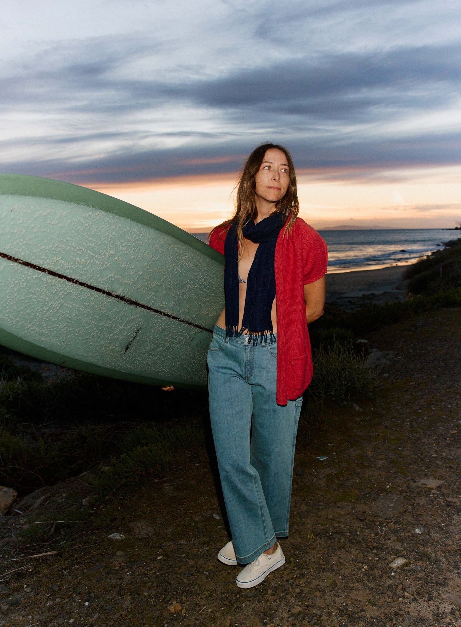 Person standing on a beach with a surfboard at sunset