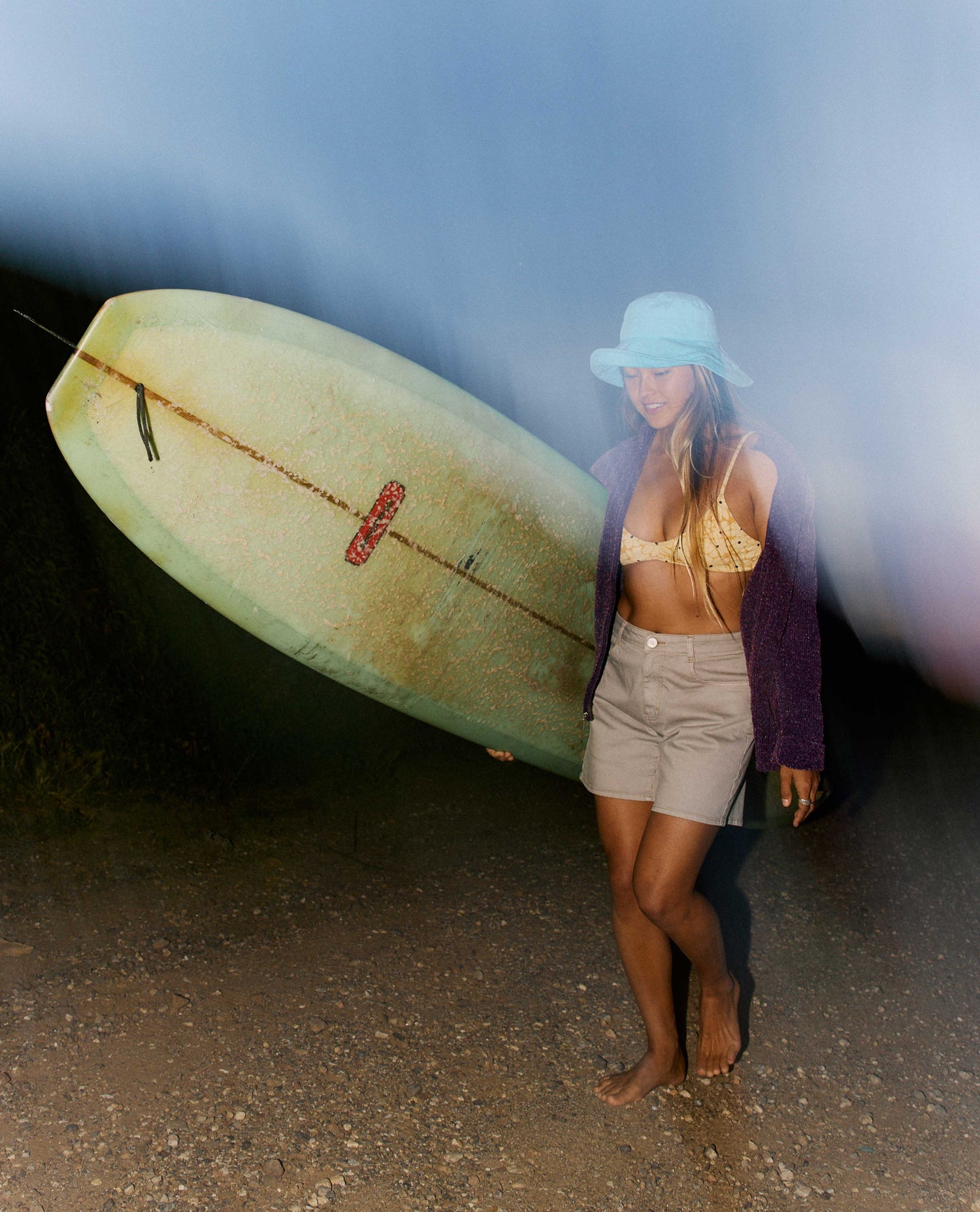 Woman holding a surfboard on a beach with a blue sky