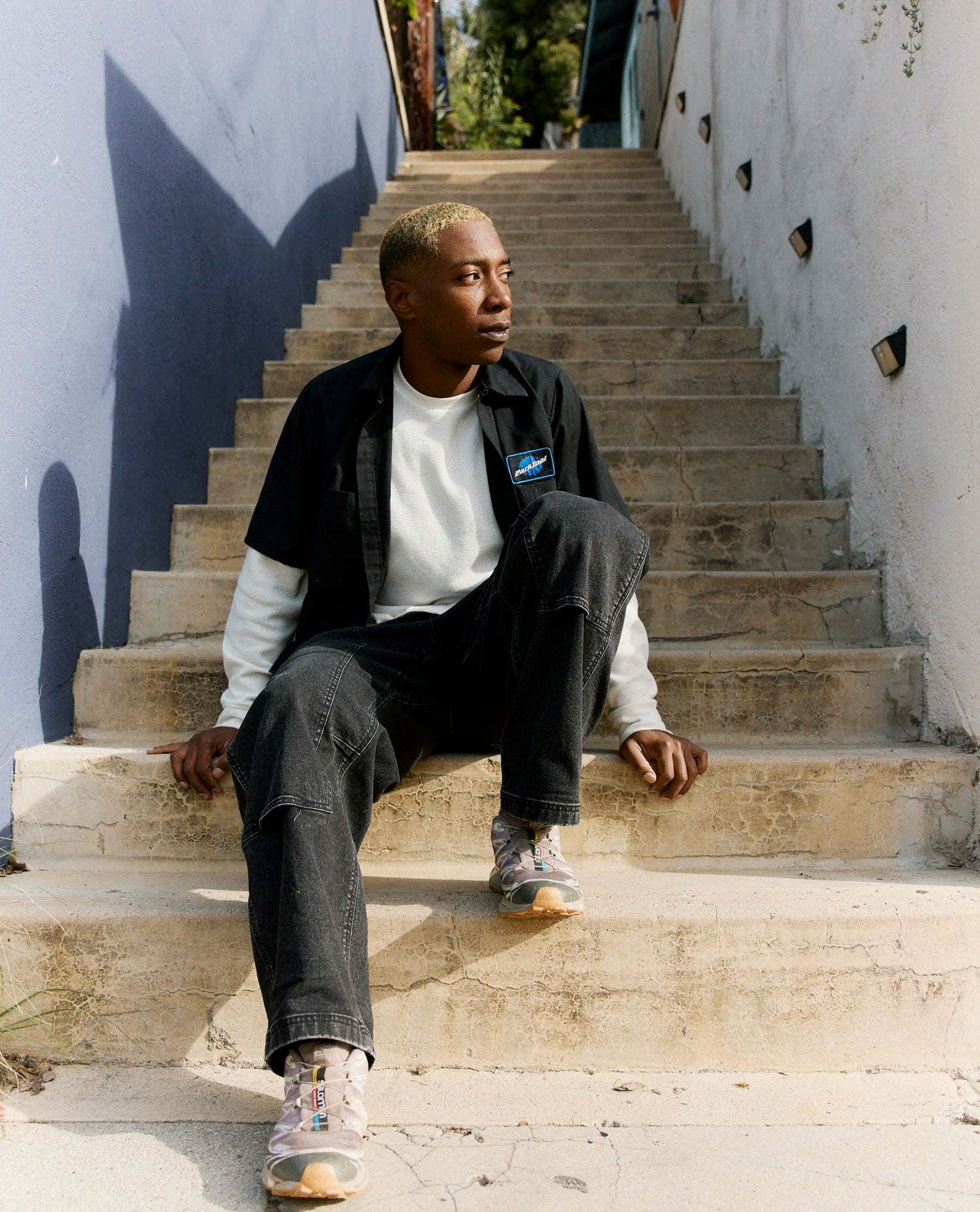 Man sitting on concrete steps with a white wall and greenery in the background