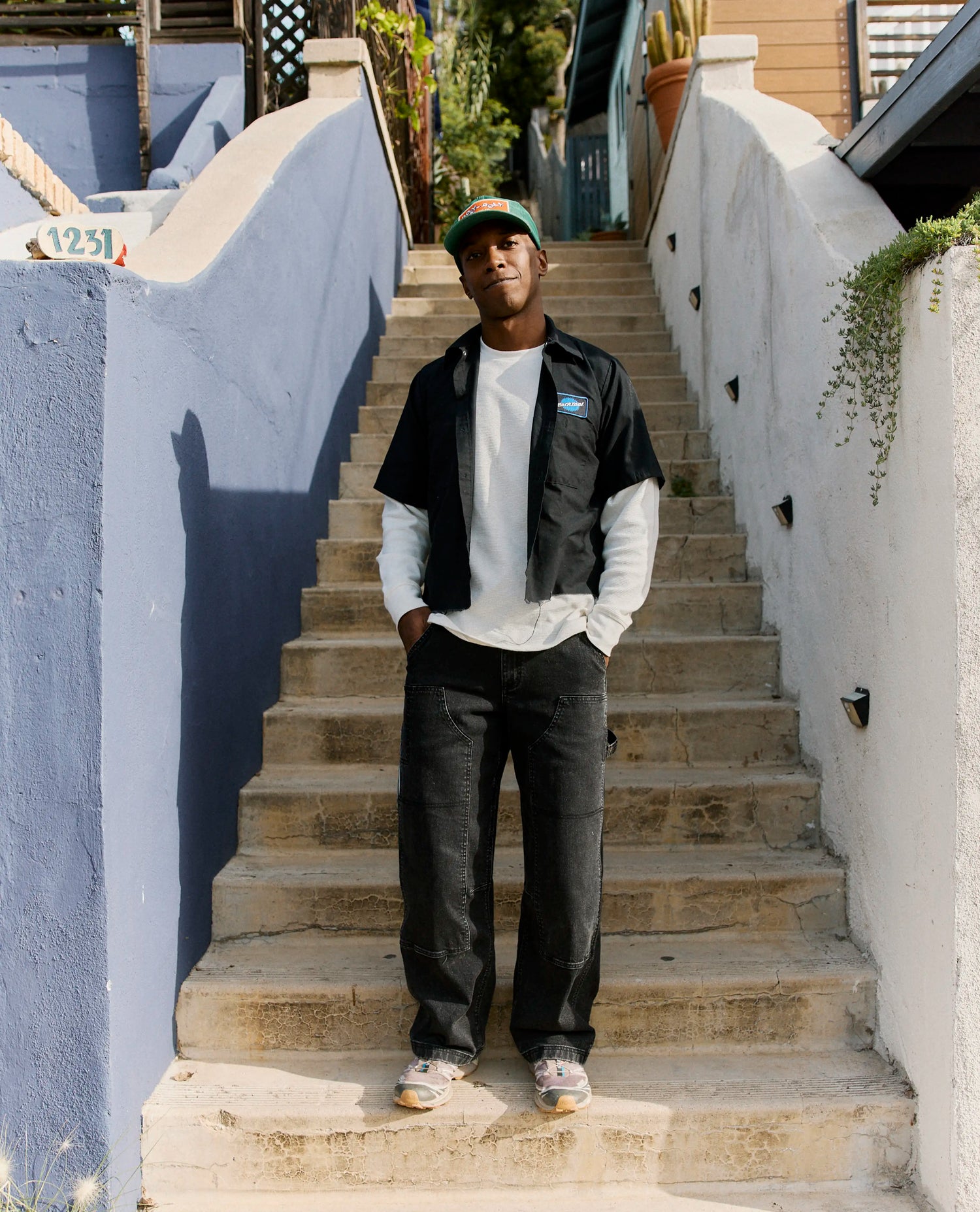 Man standing on a set of outdoor stairs wearing a black vest and white shirt.