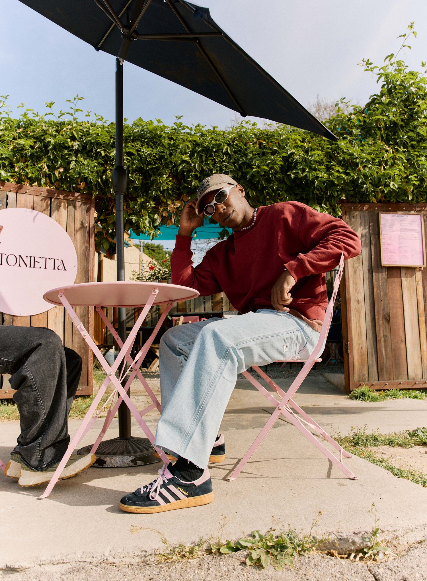 Person sitting at a pink table outdoors with greenery and a sign in the background