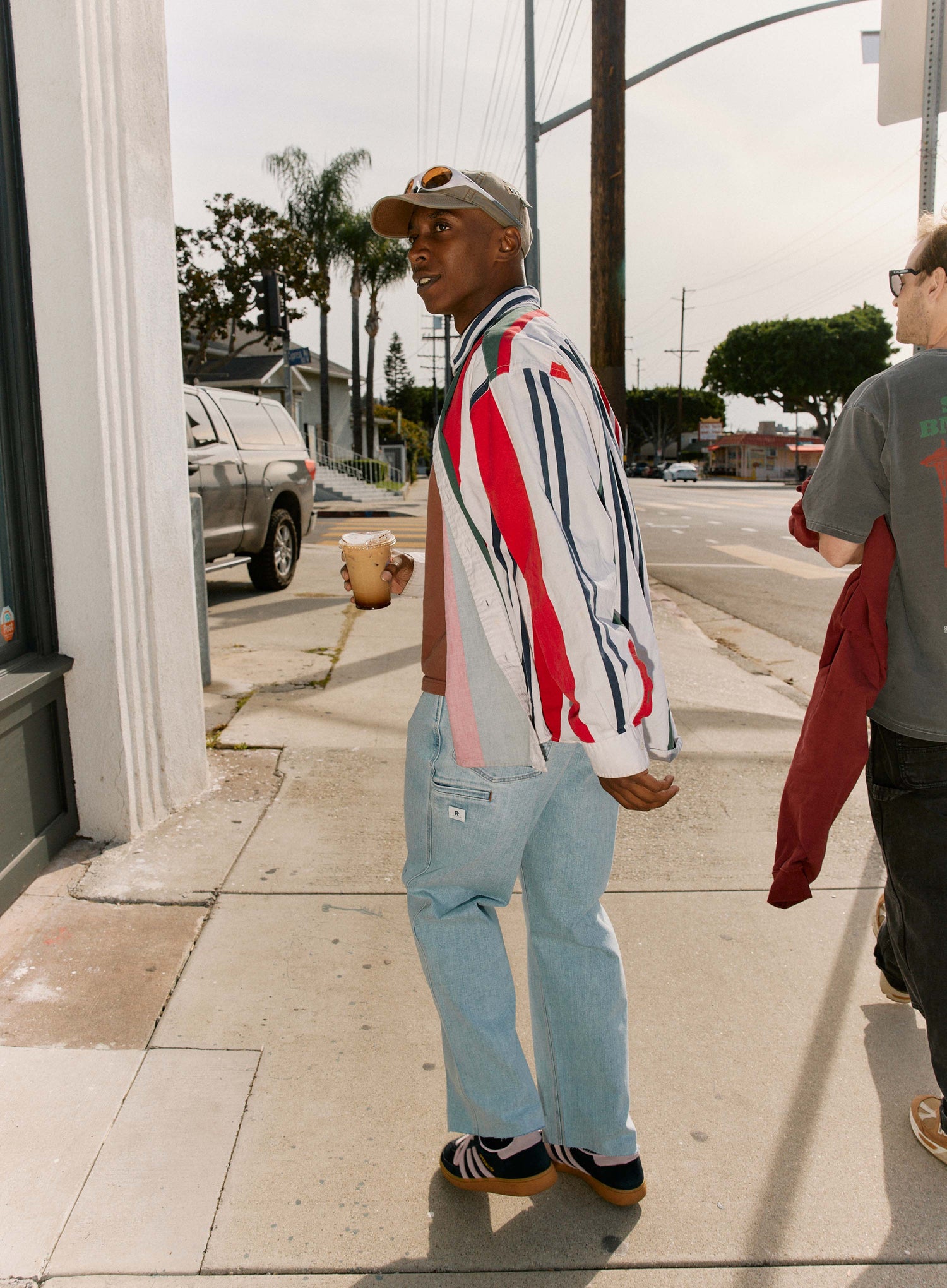 Man walking on a sidewalk wearing a colorful striped jacket and light blue jeans.