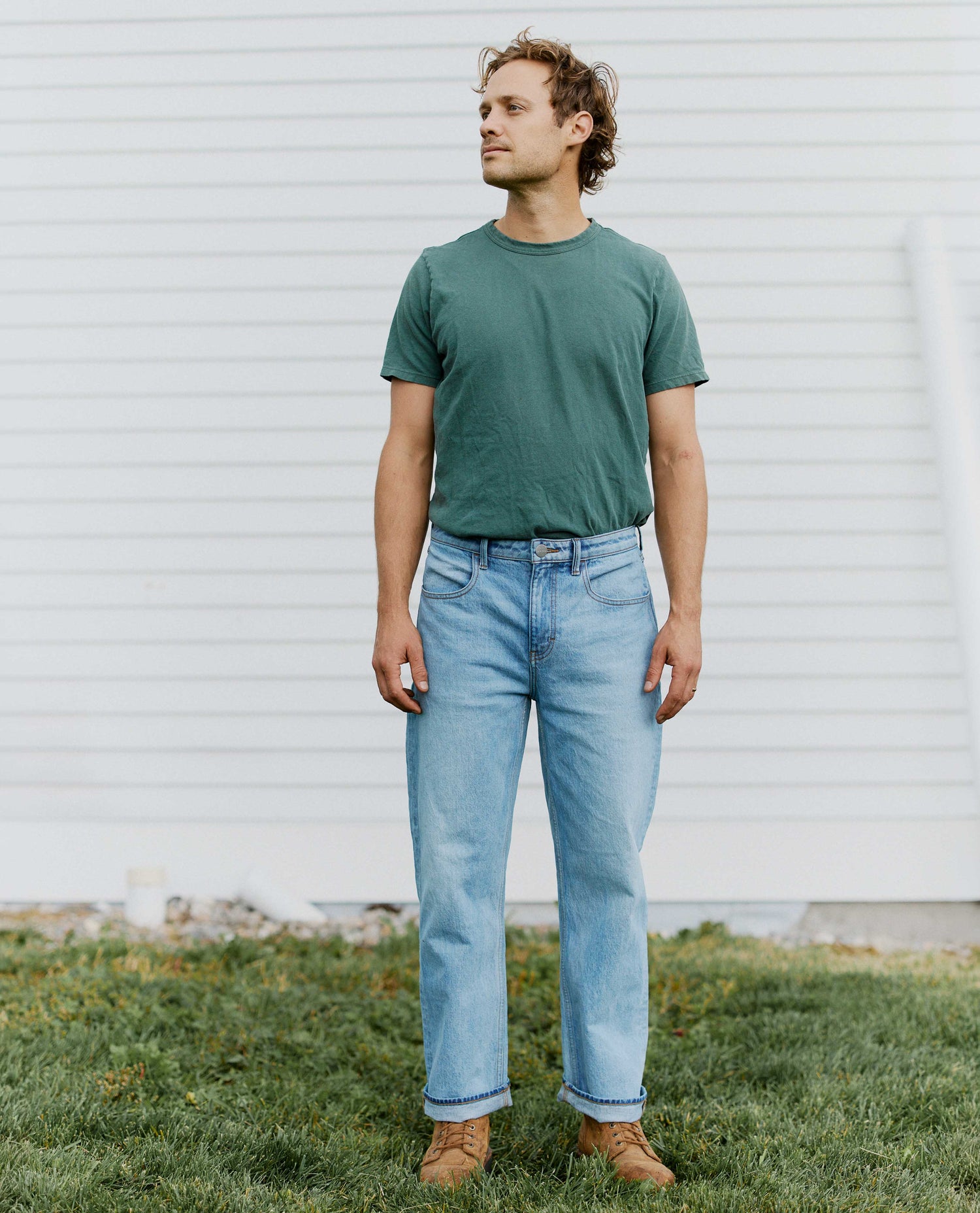 Man standing in front of a white building wearing jeans and a green tee