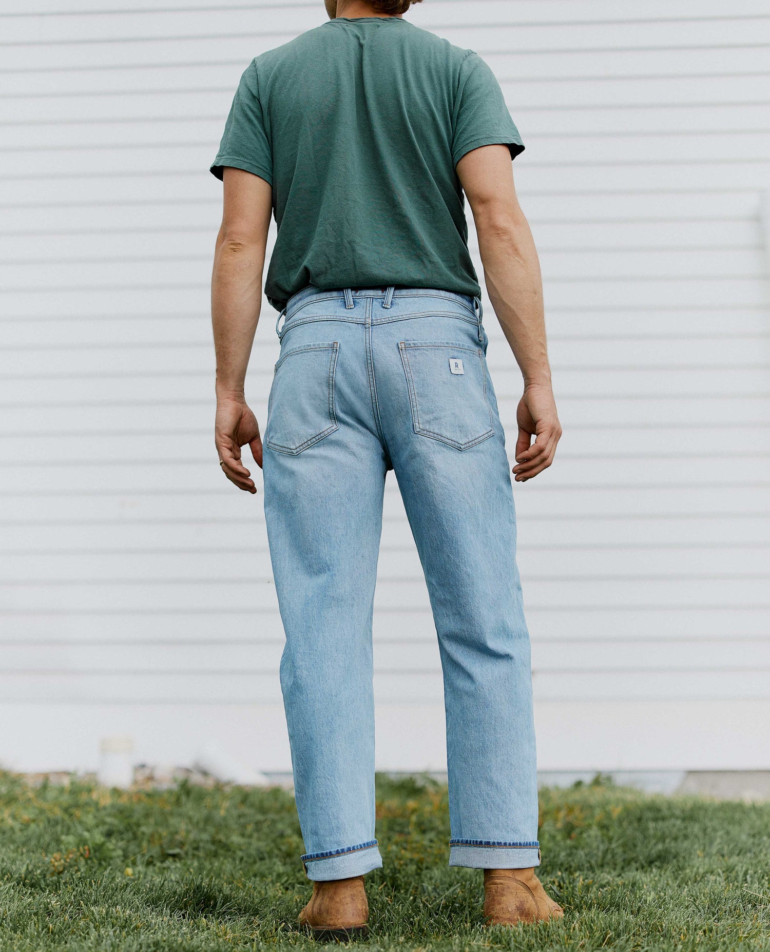 man facing away from the camera wearing light blue jeans and a green shirt