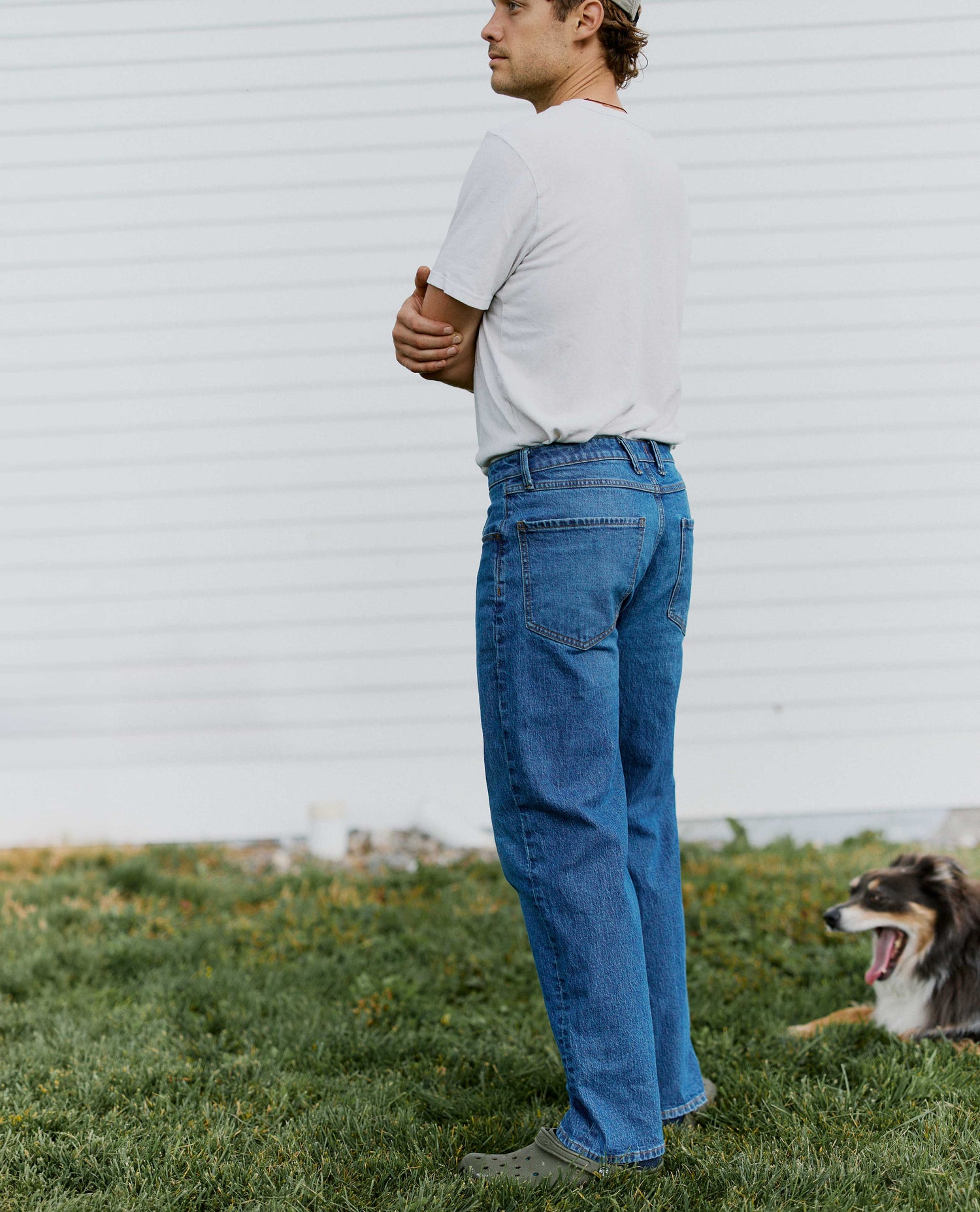 Man turned sideways wearing jeans and a white tee with a dog lying by him