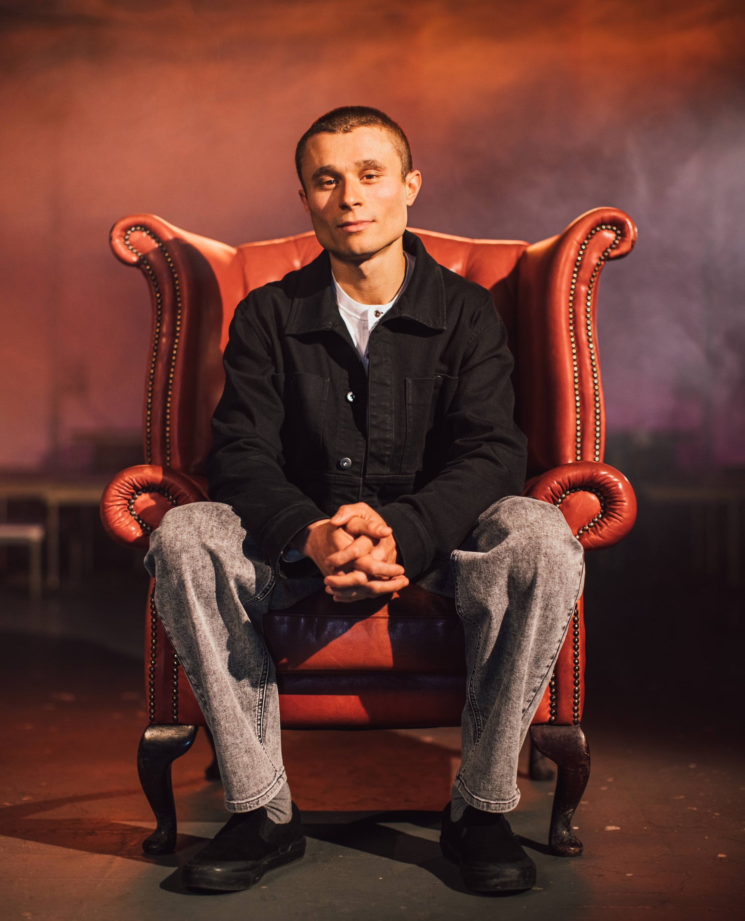 Man sitting in a red victorian style chair in Ripton 3dumb trousers. 