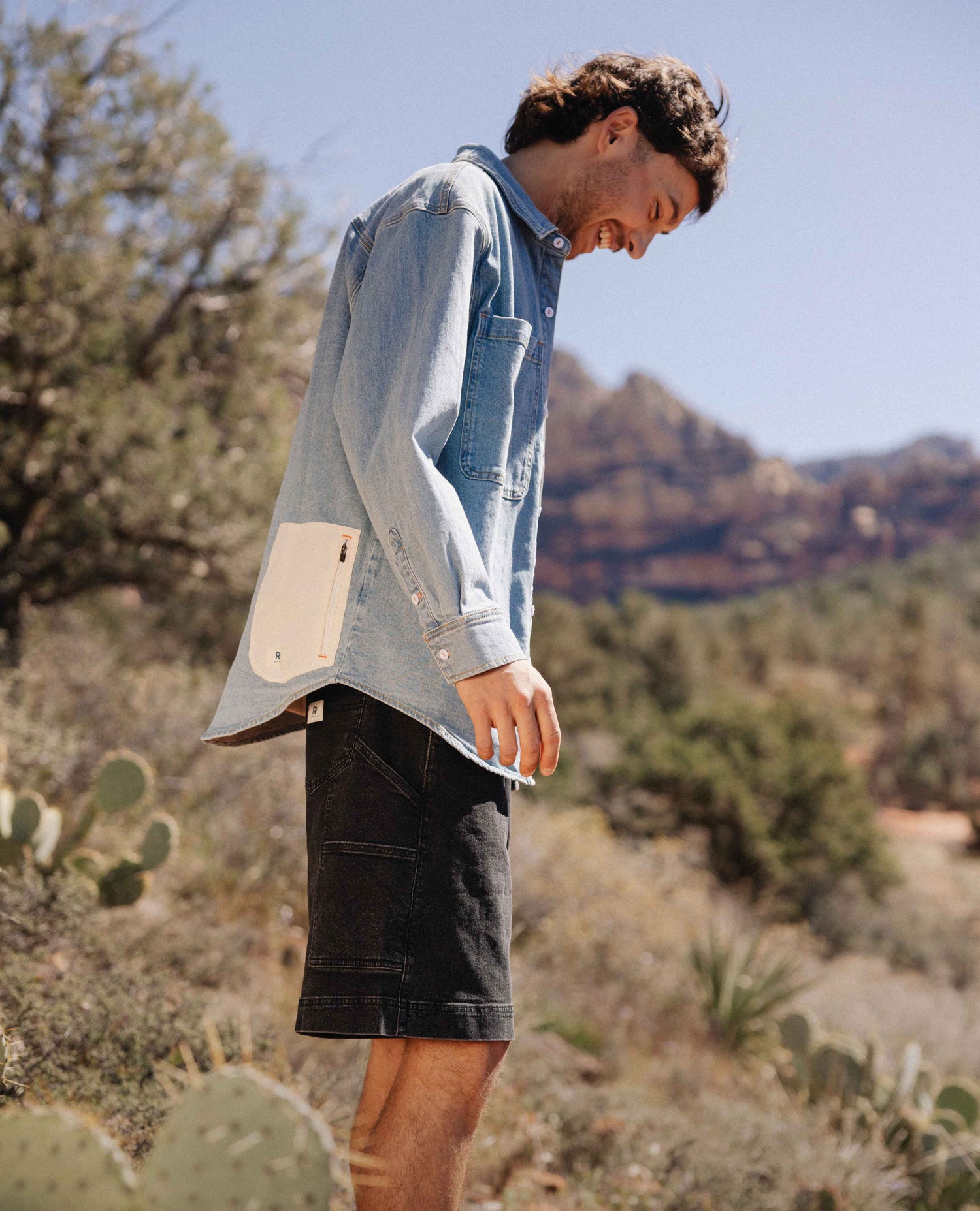 Person wearing a light blue denim shirt with beige patch in a desert setting