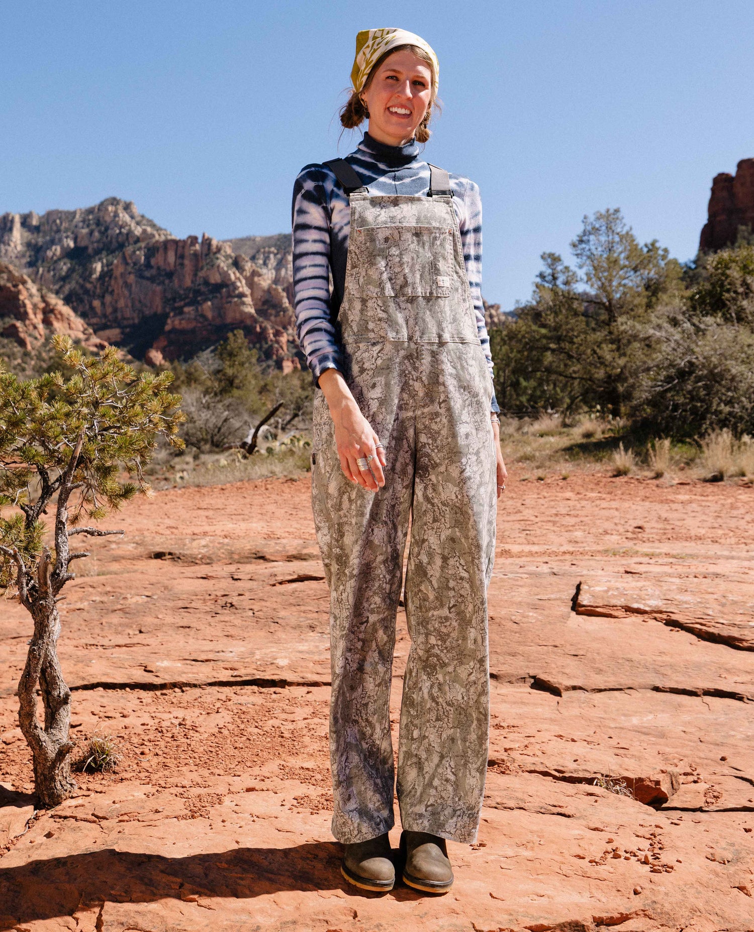 Person wearing a patterned outfit standing in a desert landscape with red rock formations.