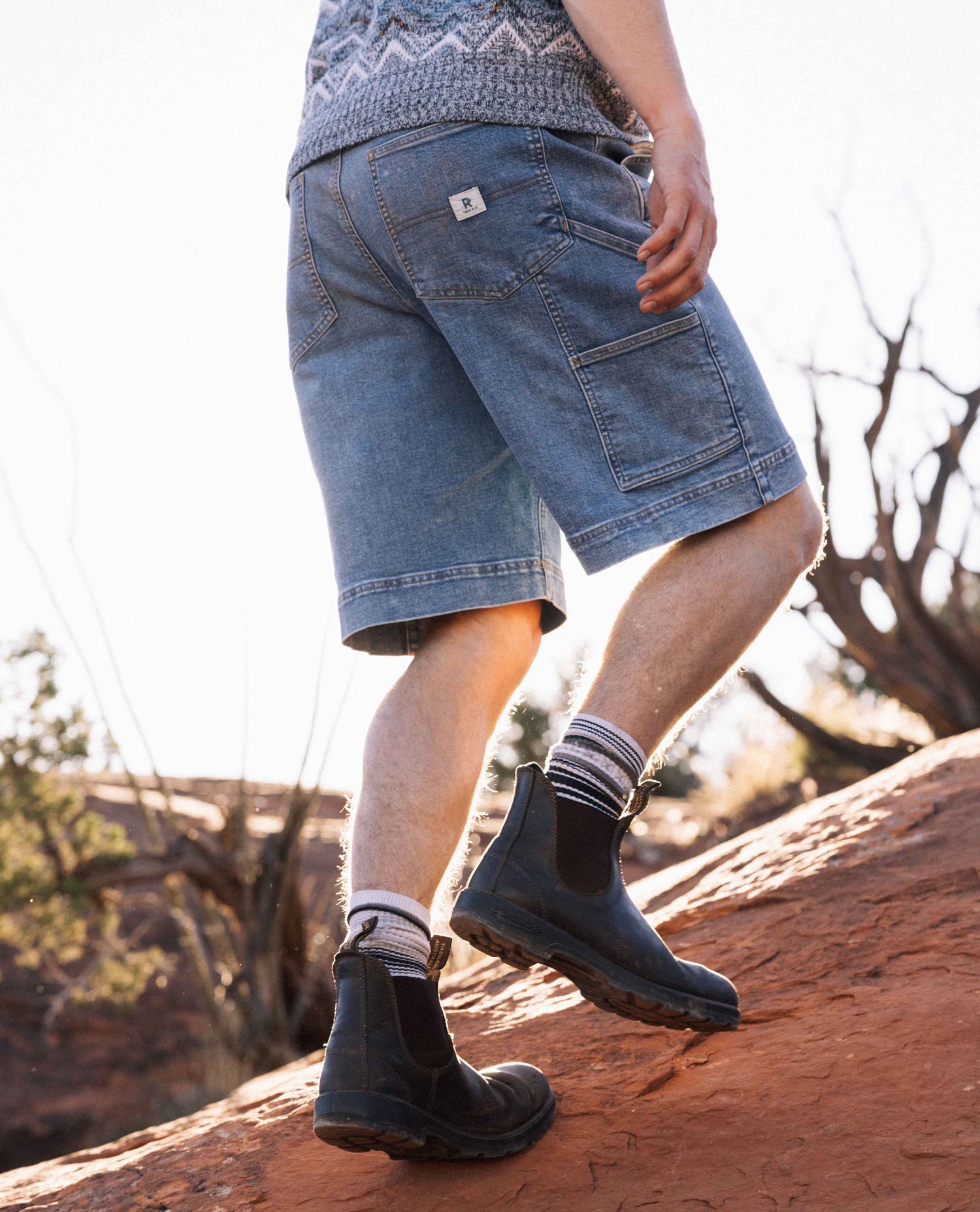Person wearing blue shorts and black boots standing on a rock with a natural landscape background